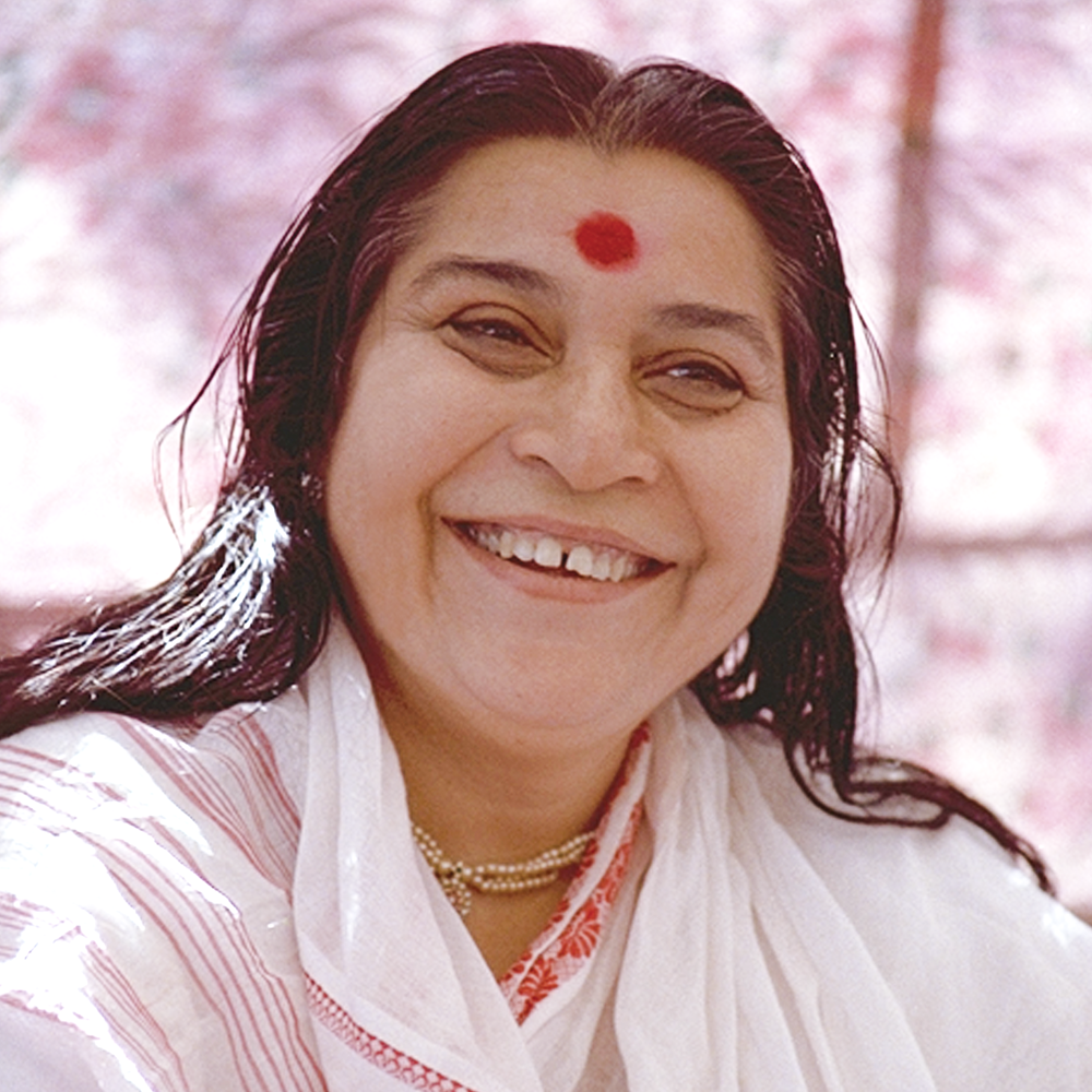 Close-up of a smiling woman with dark hair, wearing a white traditional outfit and a red bindi on her forehead, outdoors with pink blossoms in the background.