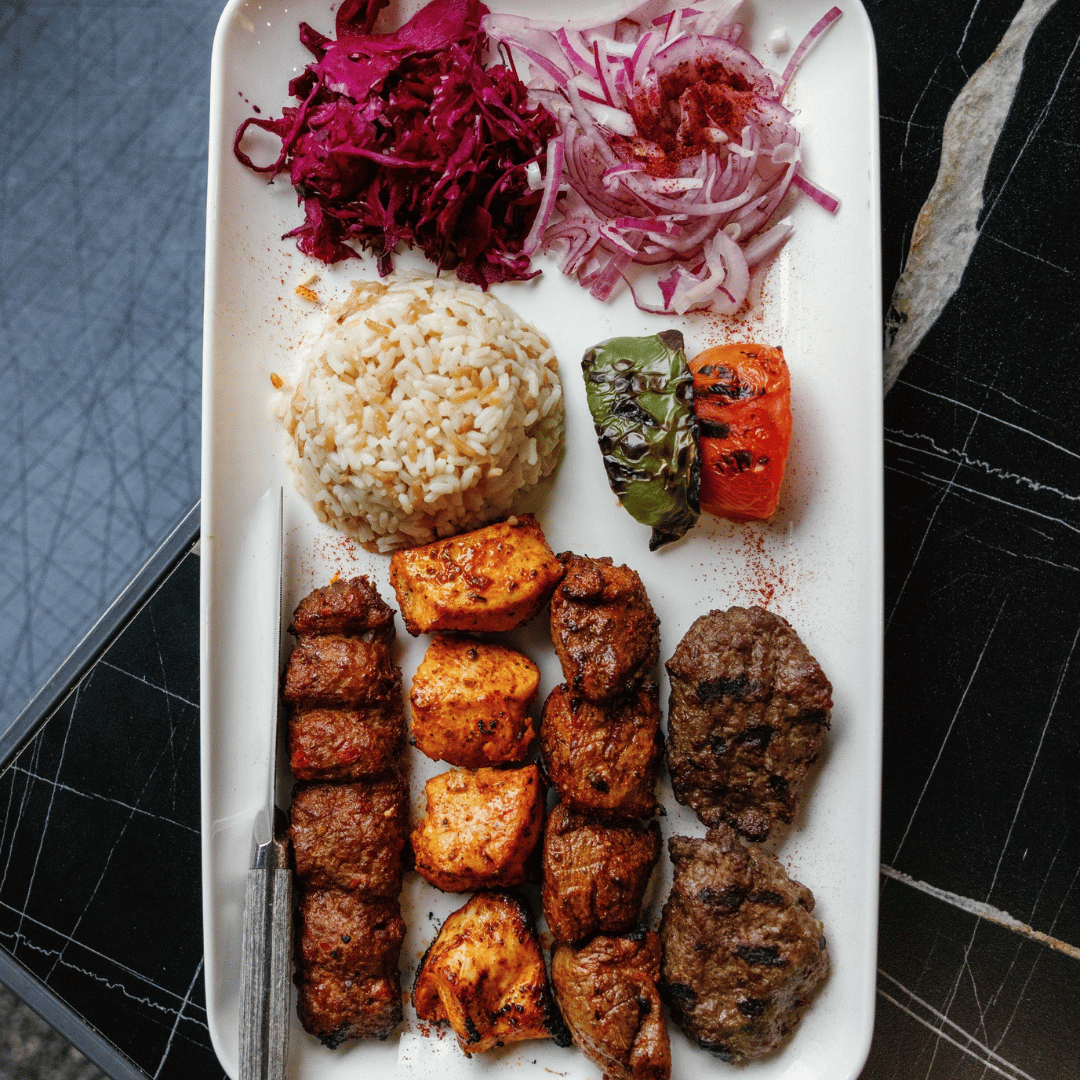 Plate with grilled meat skewers, rice, grilled vegetables, and sliced red onion and purple cabbage salad.