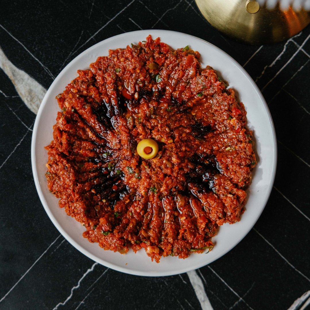 Plate of chili con carne garnished with a green olive in the center, on a black marble surface.