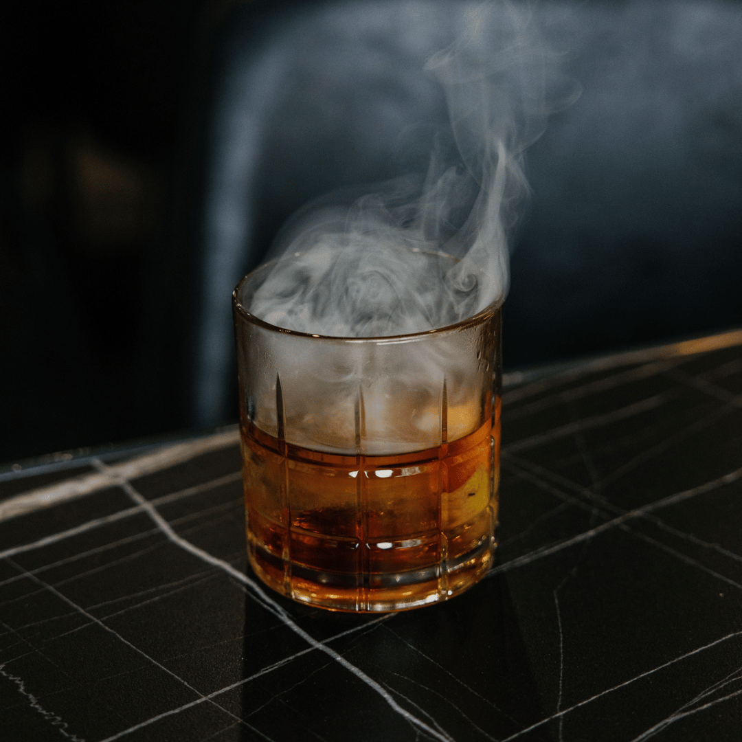 A glass with a drink, emitting smoke or vapor, on a dark surface.