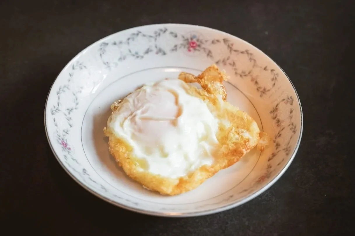Sunny side up egg with a set white and soft yolk, lightly fried in a floral ceramic bowl.
