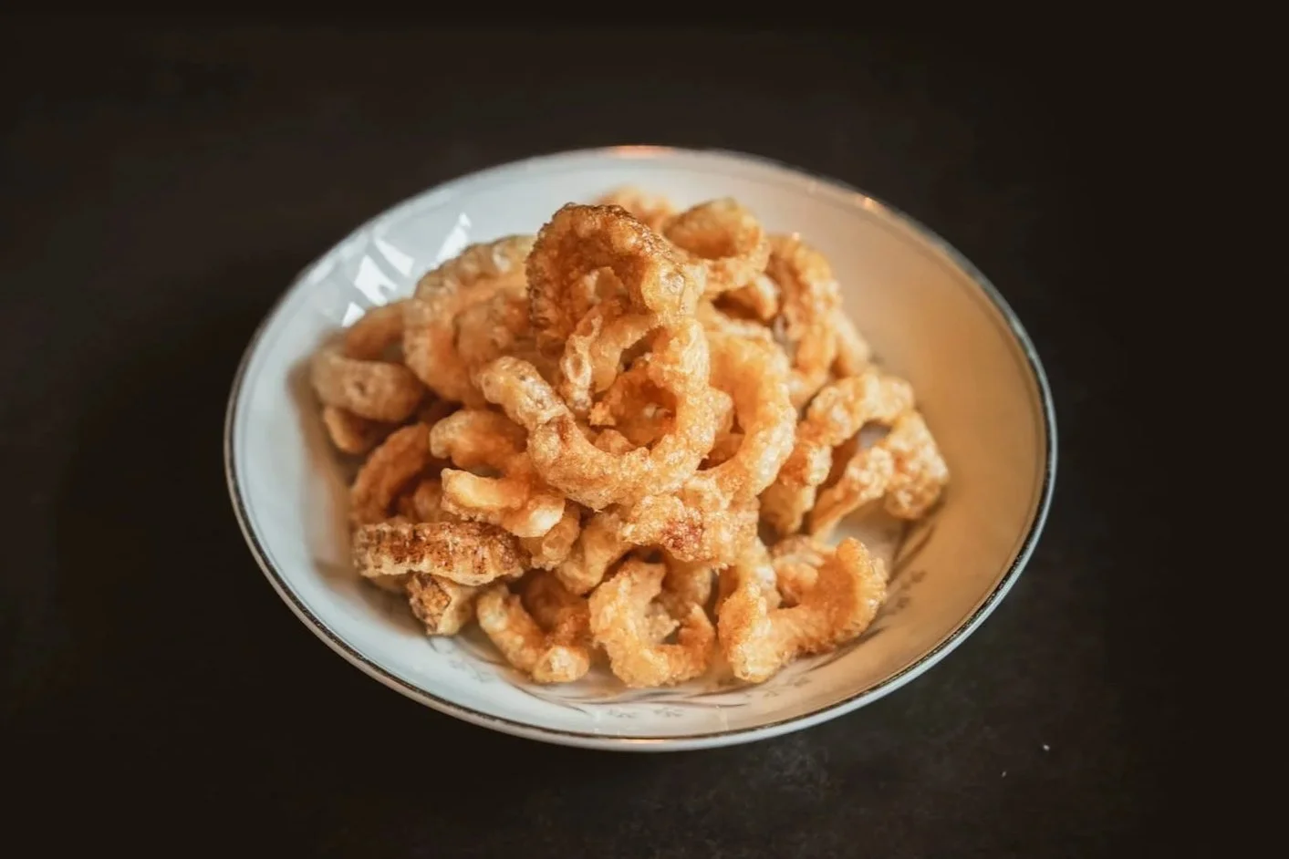 Pork Crackling piled on a round ceramic plate, golden and puffed.