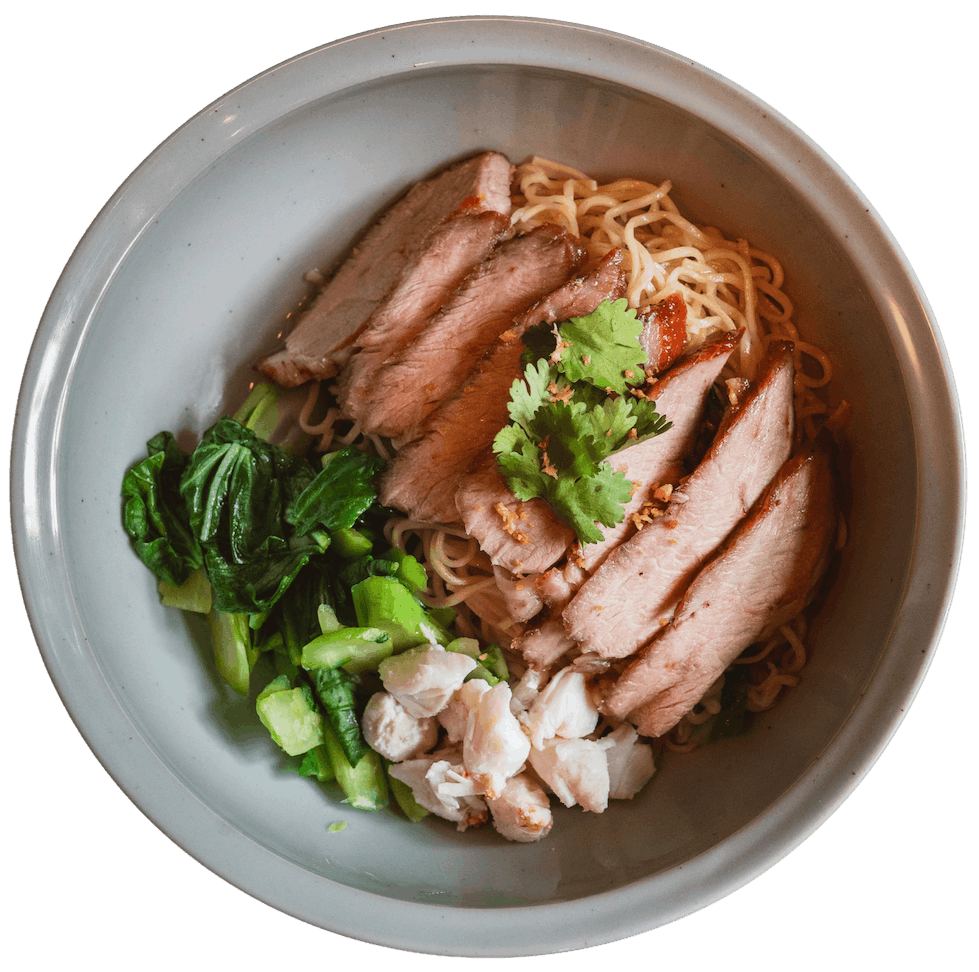 Overhead view of Ratchaburi Pork and Dry Crab Noodle in a wide bowl with sliced roasted pork, handmade egg noodles, crab meat, yu choy, and fresh cilantro.
