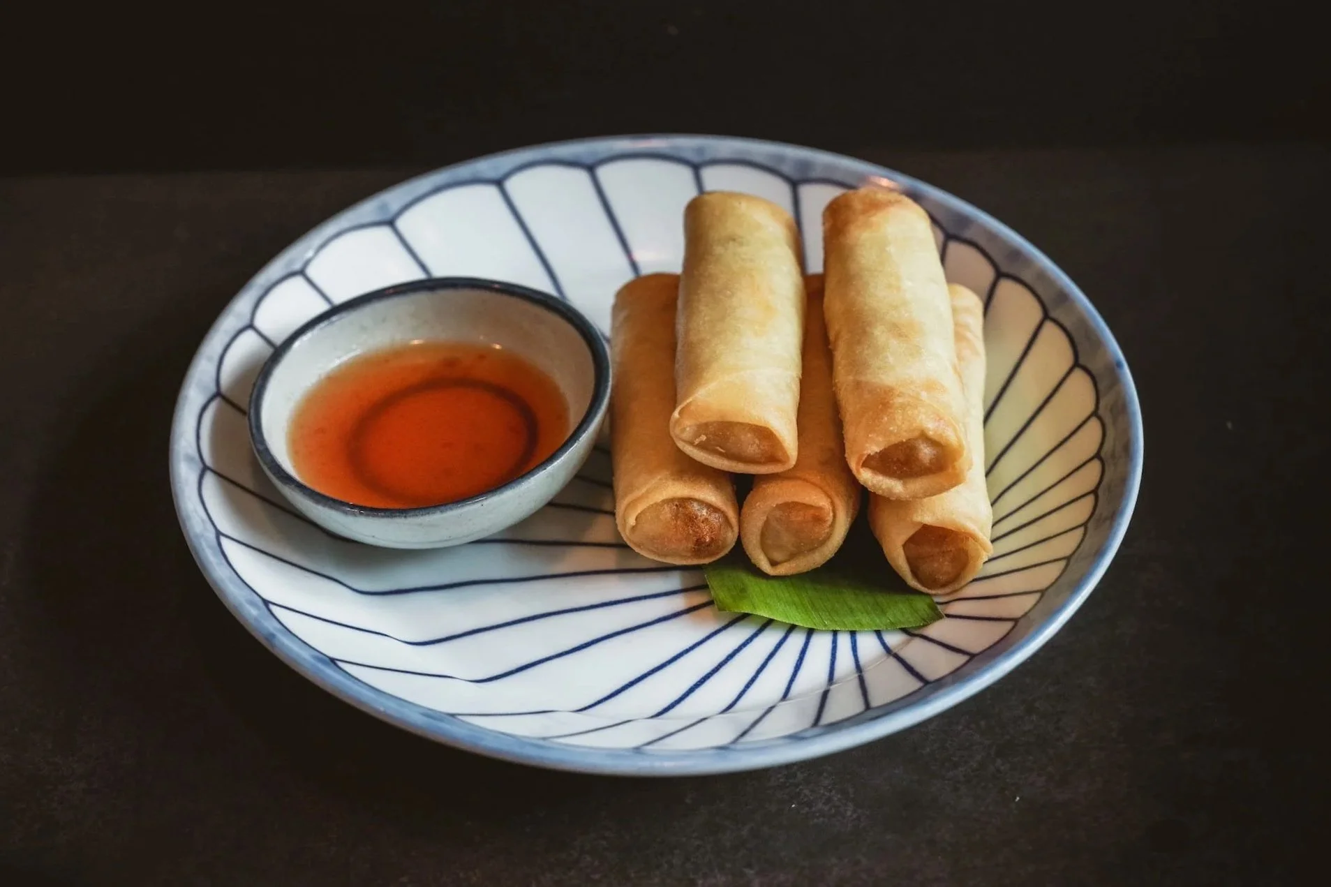 Five golden Crispy Spring Rolls on a blue and white plate with a side of Thai plum dipping sauce.