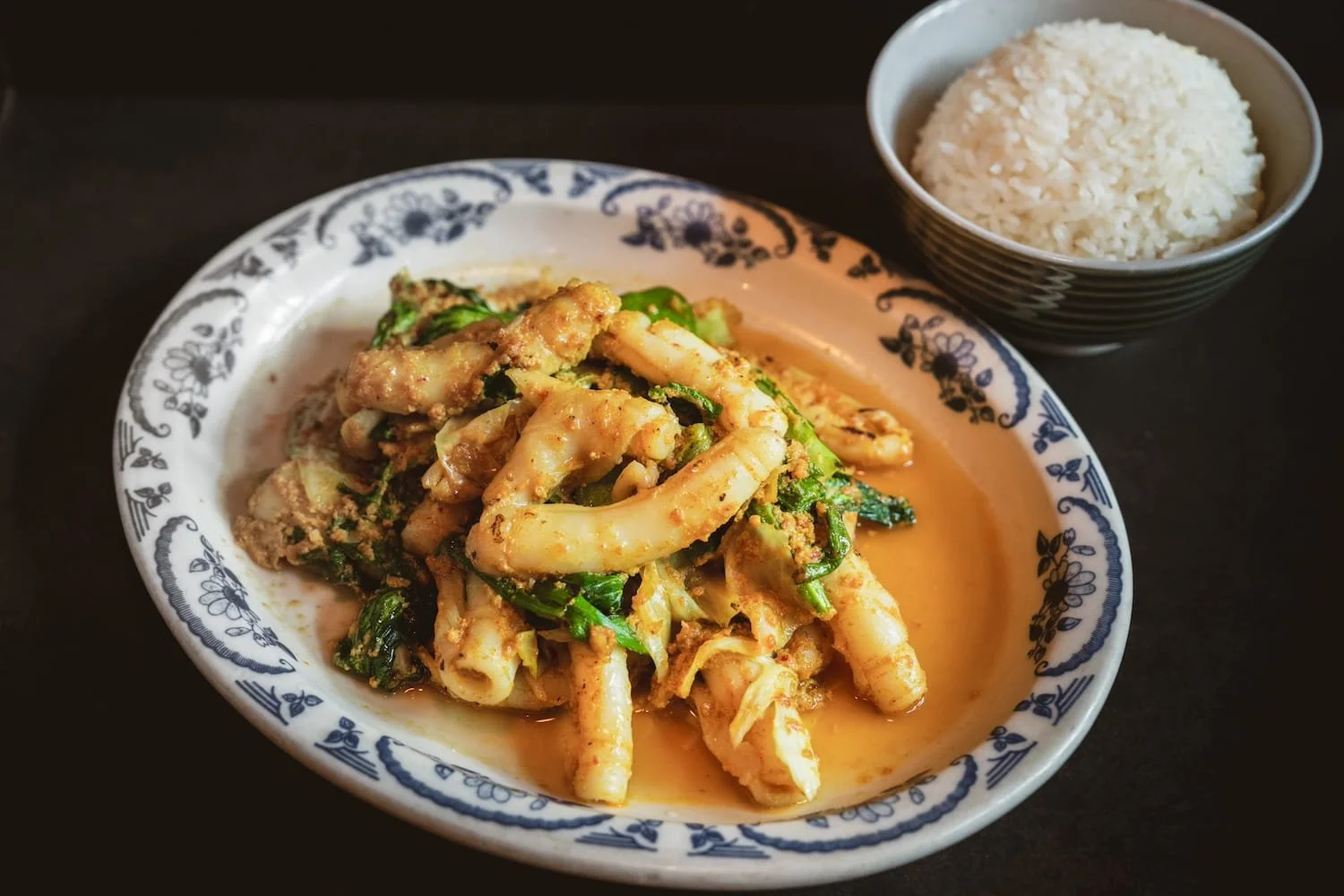 Wok Curry Paste with sliced meat, string beans, red chili, and basil in a rich curry sauce on a floral ceramic plate, served with steamed rice.