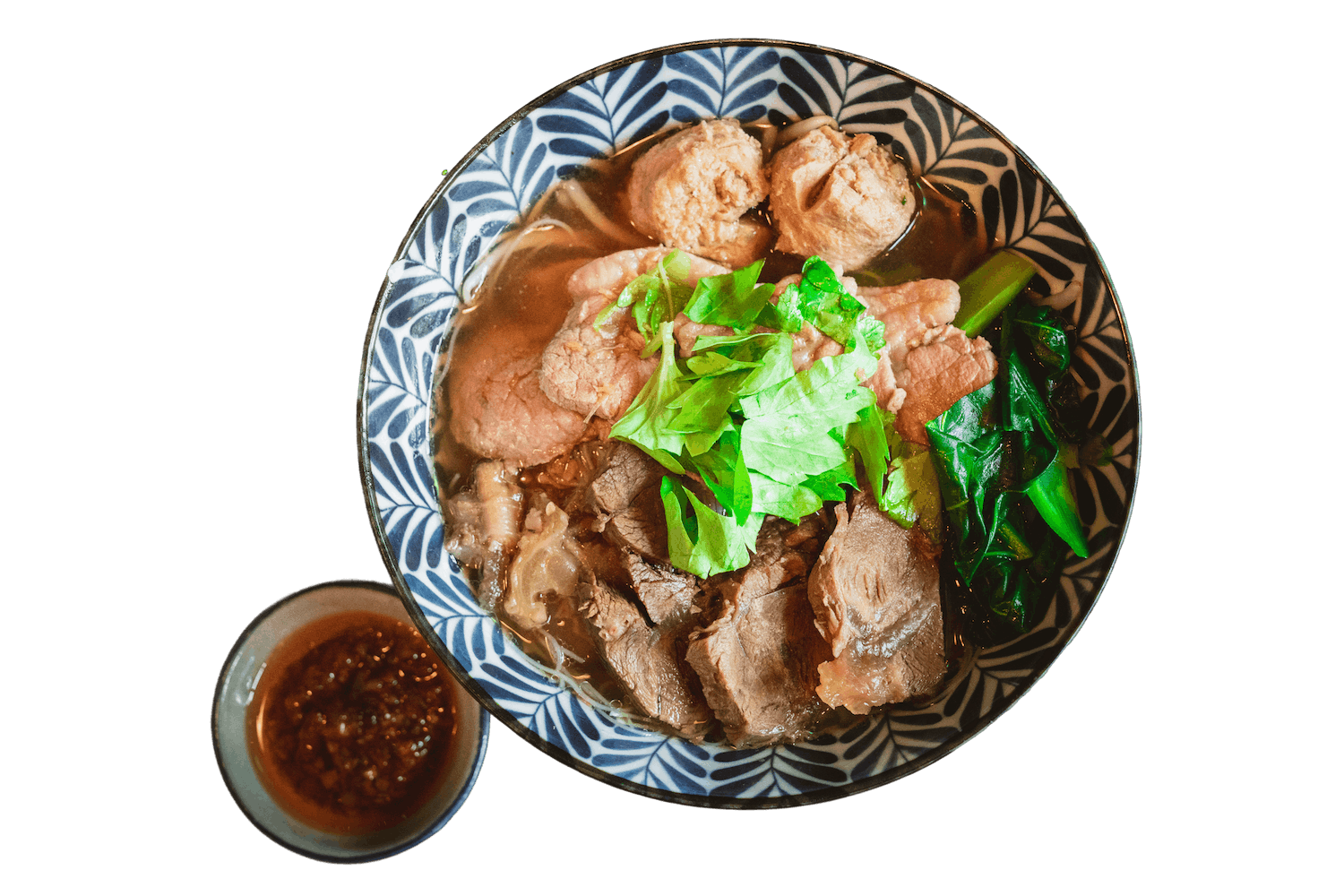 Pa-Yao Beef Noodle in a patterned bowl with braised beef, meat balls, yu choy, and Asian broccoli in a clear broth, serve with  chili sauce on the side.