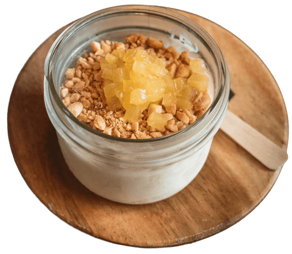 Sugarcane Ice Cream in a glass jar topped with pineapple marmalade and crushed peanuts, served on a round wooden board.