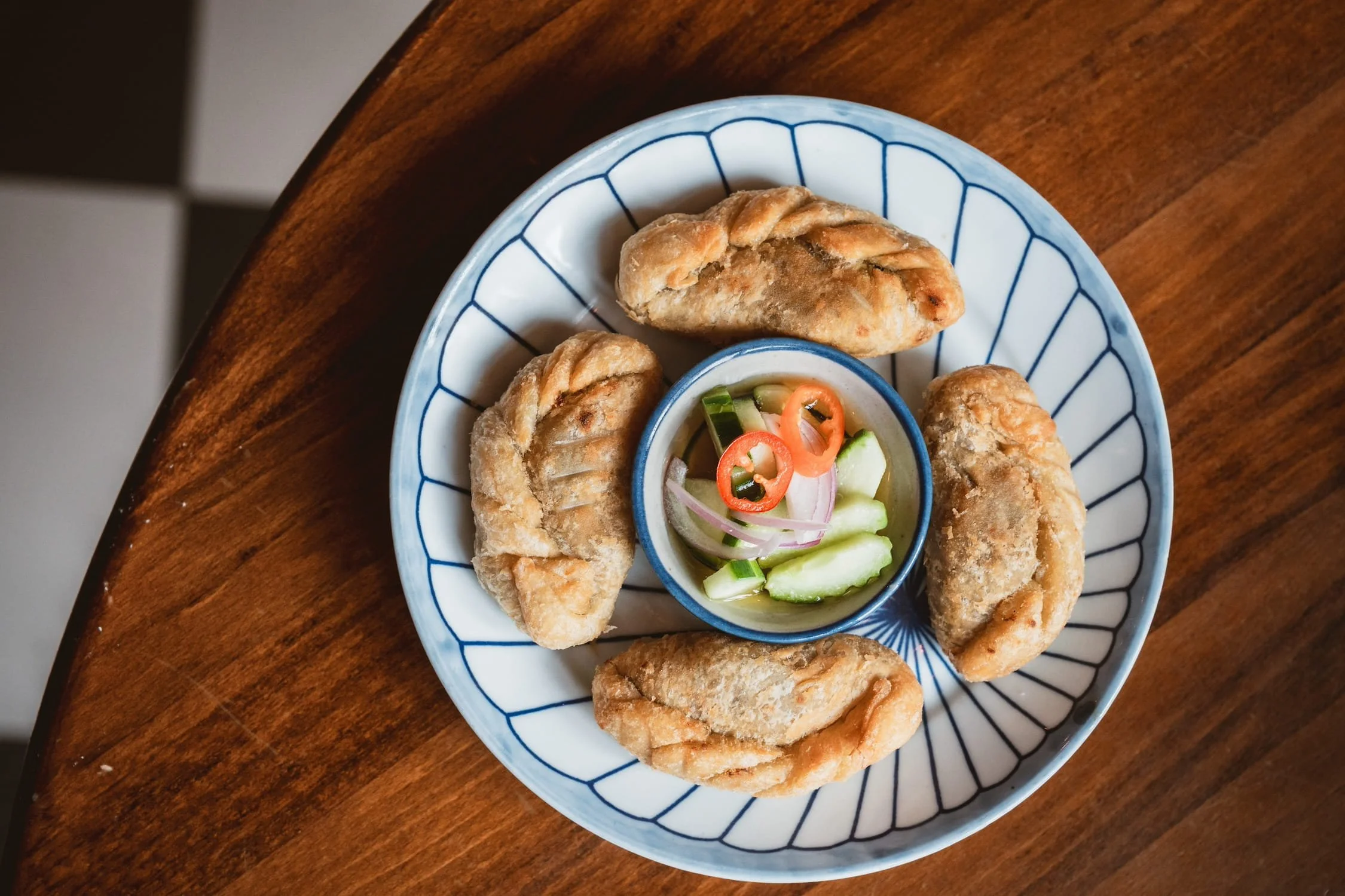 Overhead view of four Root Vegetable Puffs arranged on a blue and white plate around a small bowl of cucumber relish with sliced chili.