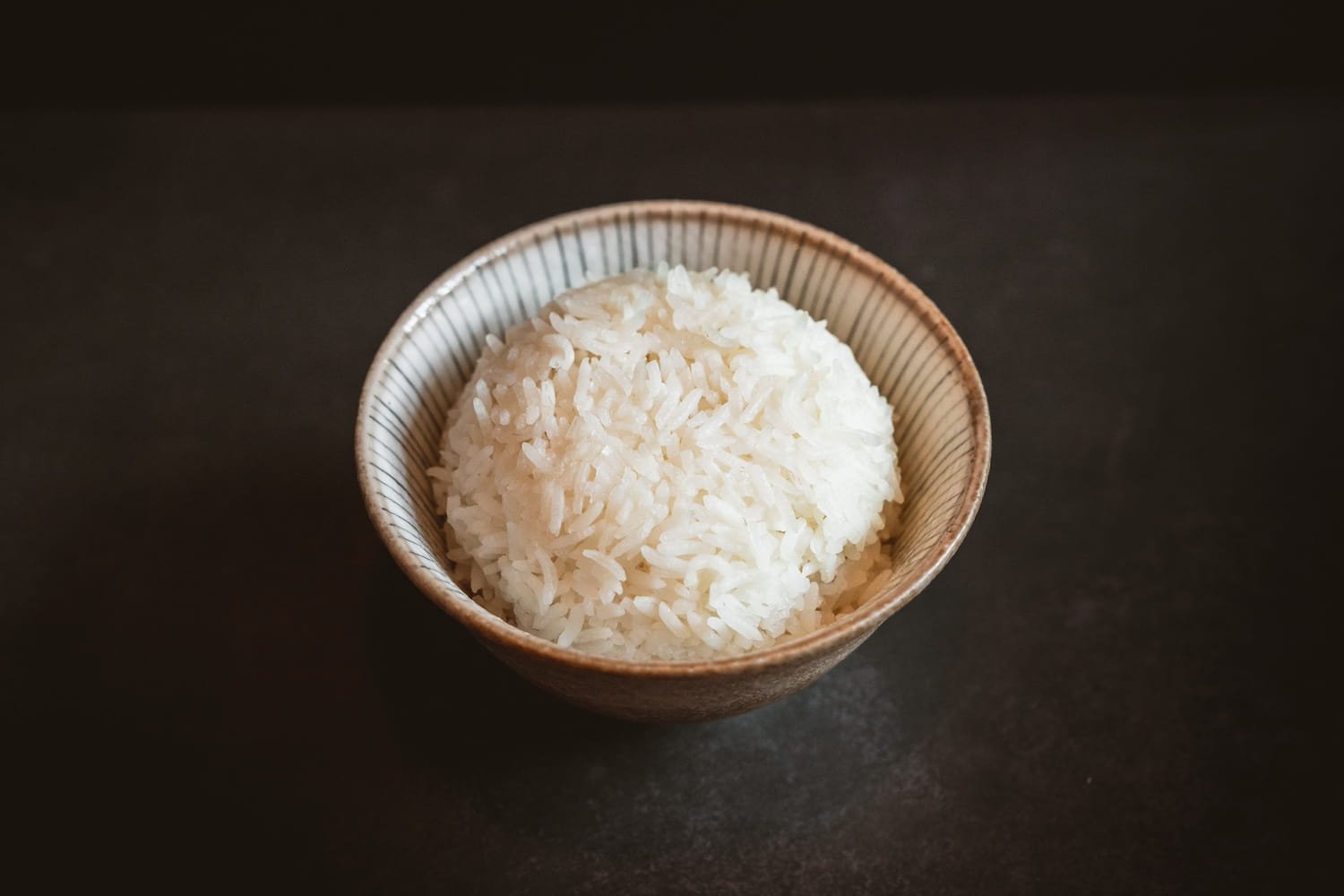 A bowl of steamed jasmine rice in a striped ceramic bowl.