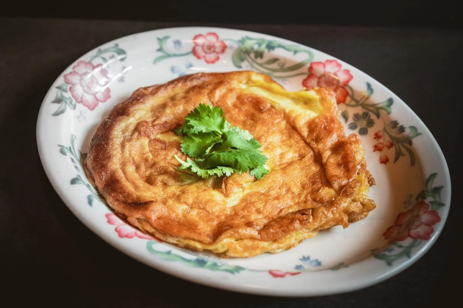 Egg Omelette with Shallot, golden and crispy-edged, garnished with fresh cilantro on a floral ceramic plate.