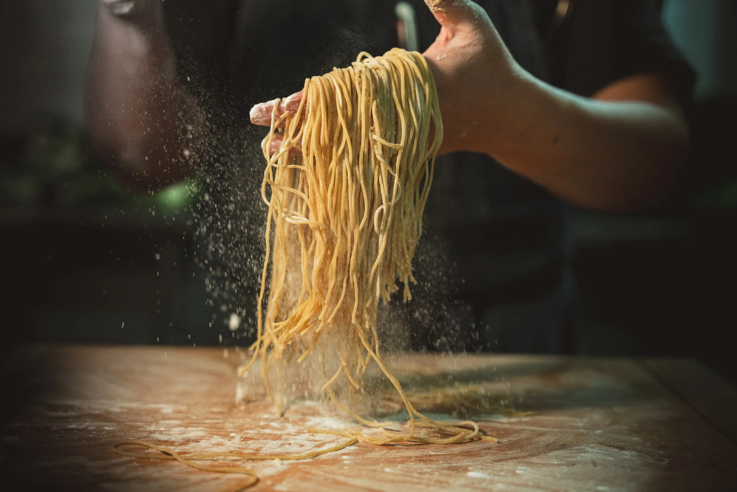 Fresh noodles being tossed in flour by hand on a work surface
