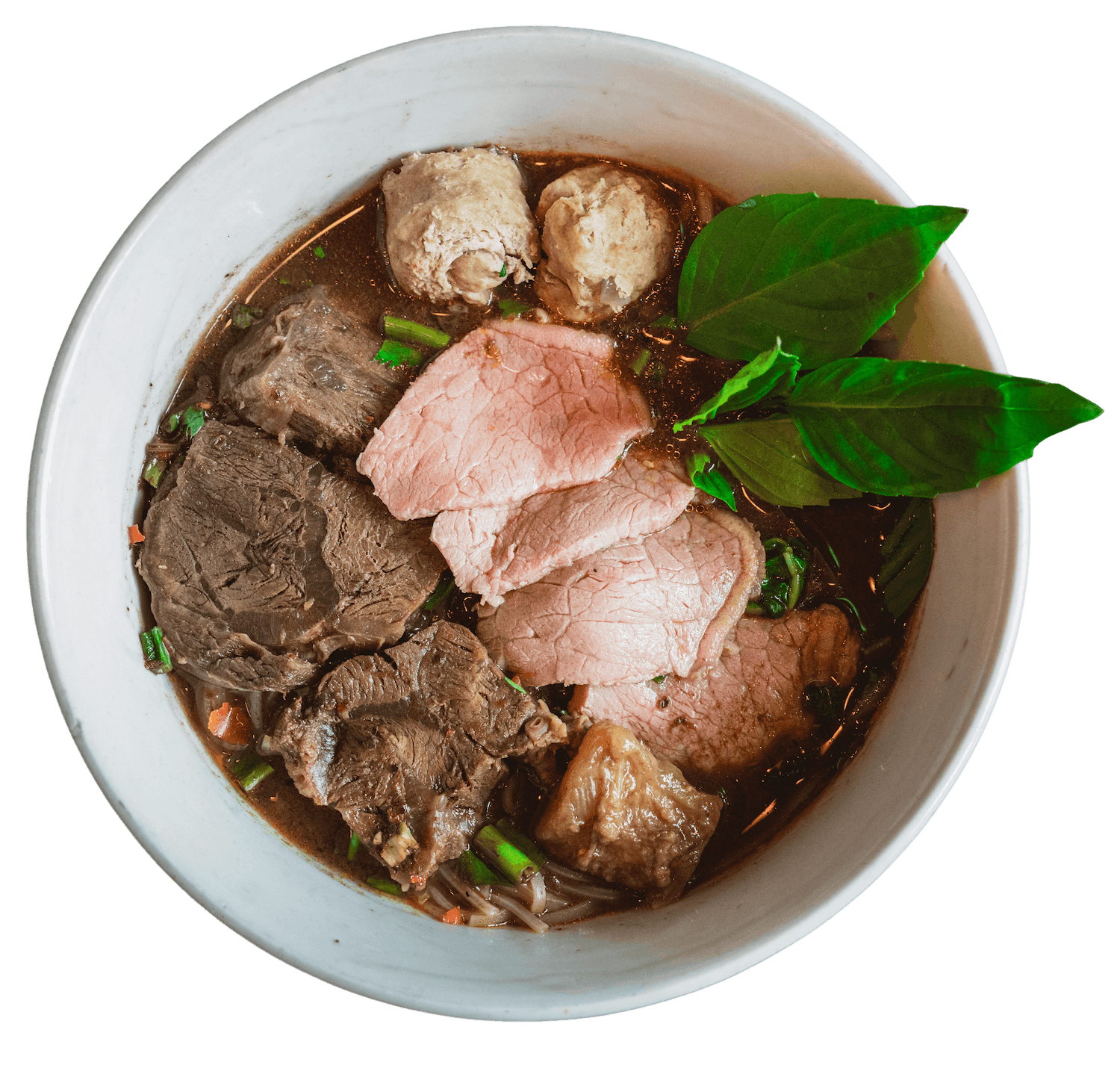 A bowl of Ayutthaya Boat Noodle with beef slices, meatballs and garnished with basil.