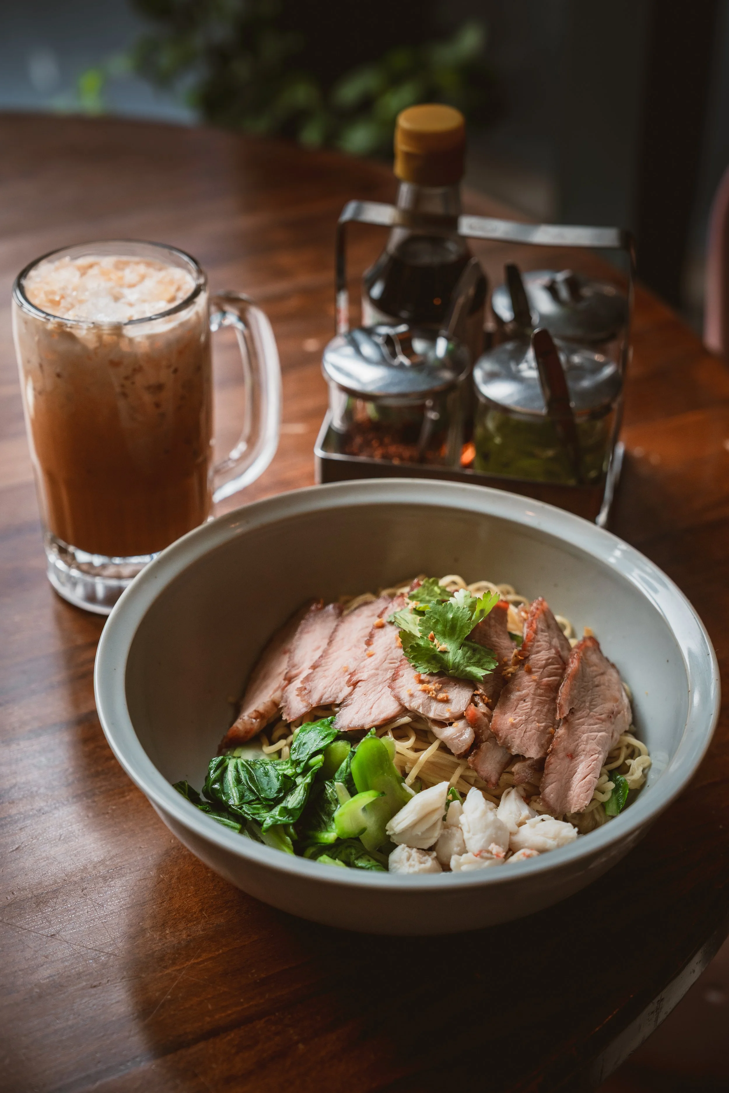 Ratchaburi crab and pork dry noodles with roasted pork, crab, herbs, Thai milk tea, and condiments.