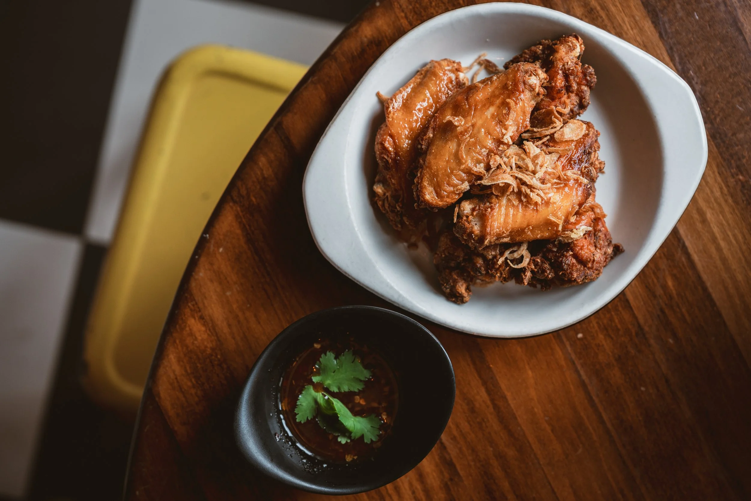 Plate of crispy fried chicken with a side of hot sauce garnished with cilantro.