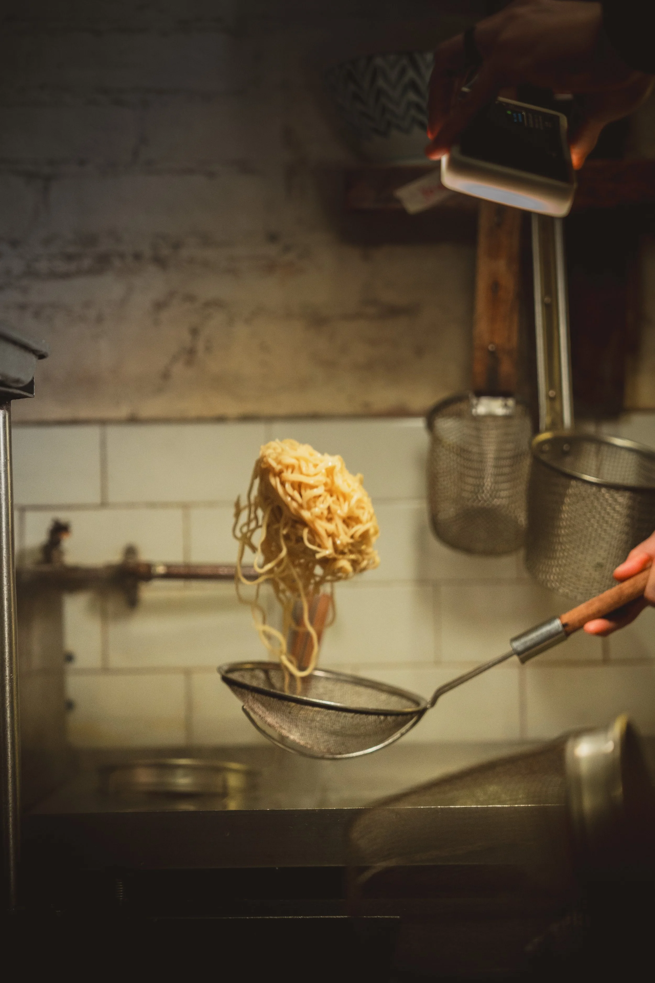 Cook lifting cooked noodles from boiling water with a strainer.