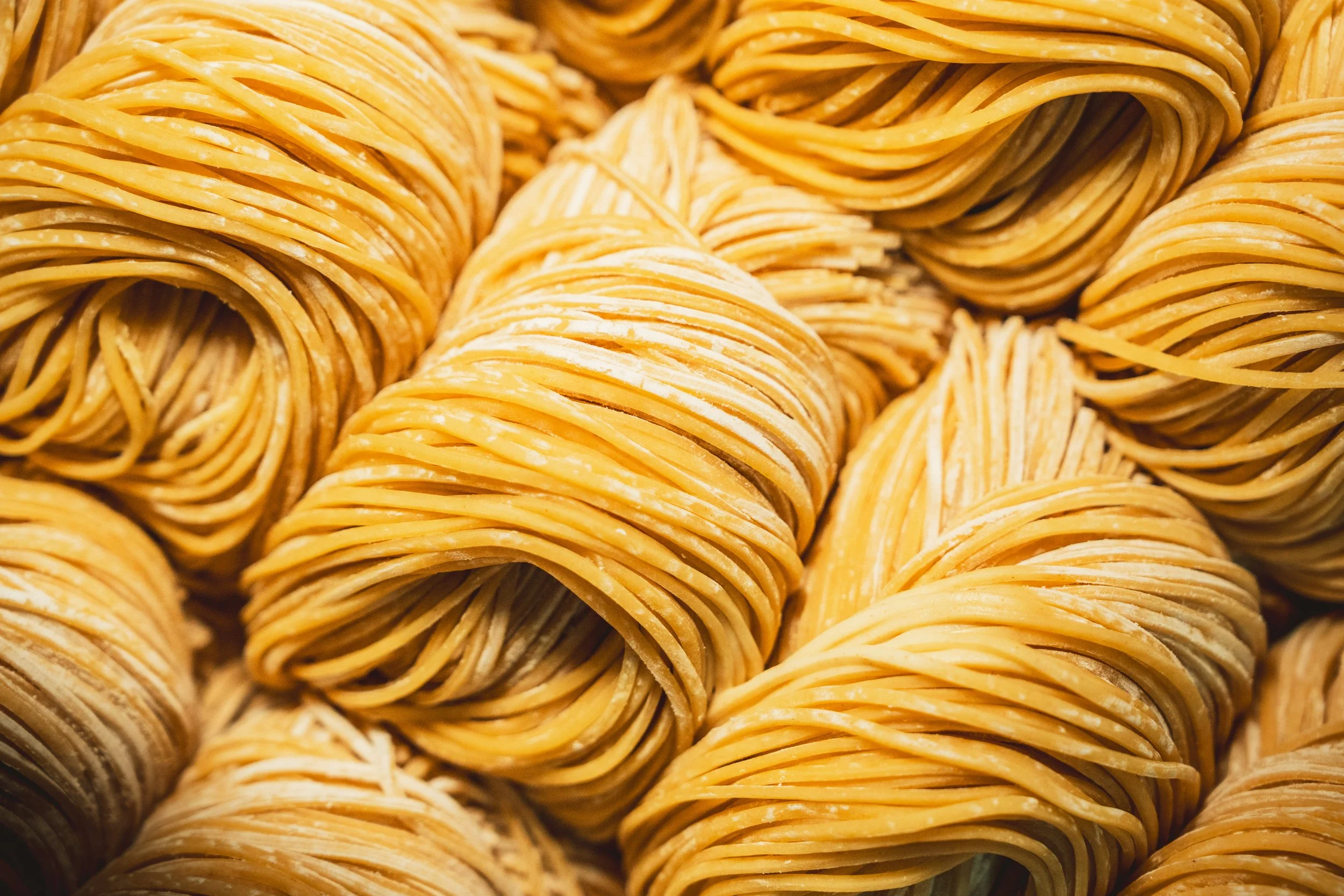 Fresh handmade egg noodles coiled into nests and dusted with flour on a wooden surface.