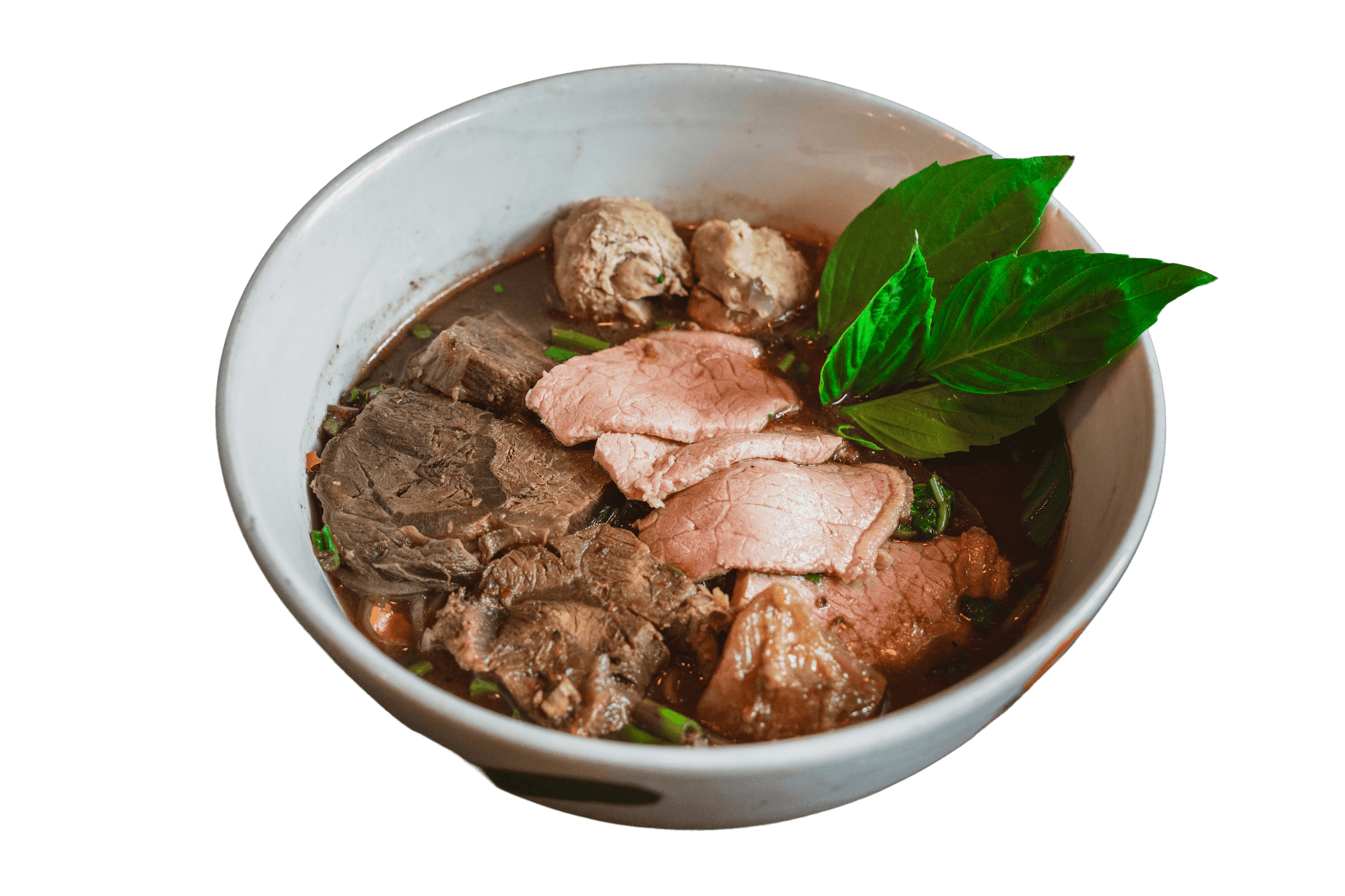 A bowl of Ayutthaya Boat Noodle topped with beef slices, meatballs and garnished with basil.