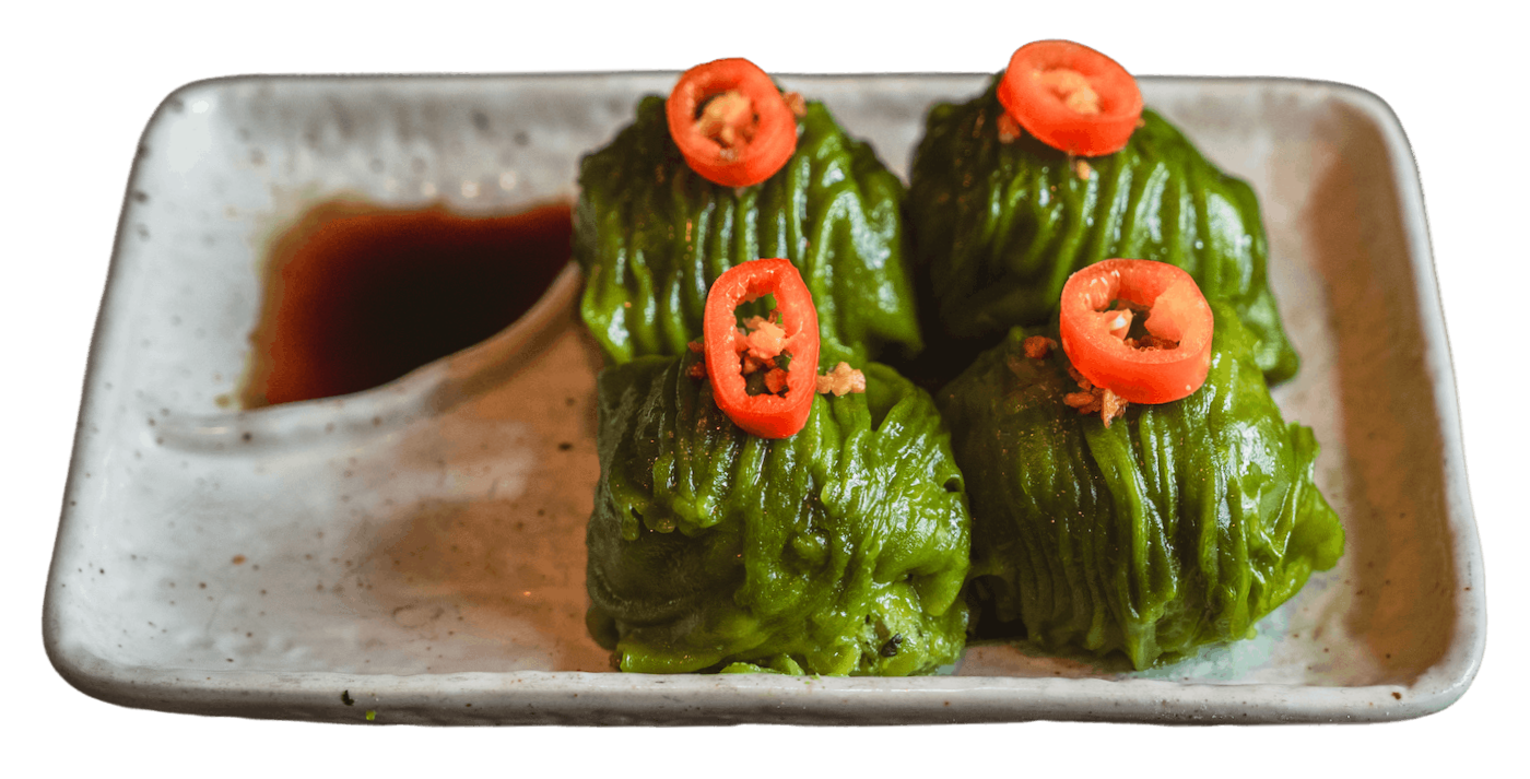 A plate of four steamed vegetable dumplings topped with chili slices and a side of soy sauce.