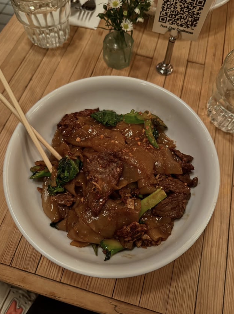 Overhead view of wide rice noodles stir-fried with beef and Chinese broccoli in dark soy sauce, served in a white bowl with chopsticks.