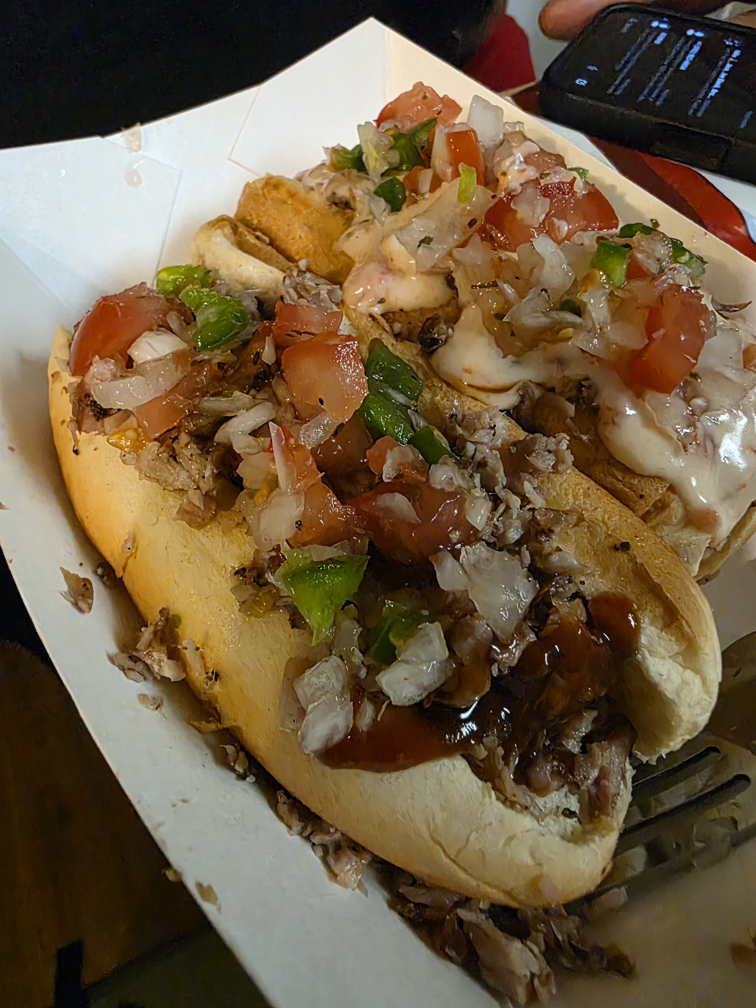 A Mexican dish called tacos loaded with chopped tomatoes, onions, green peppers, shredded meat, and topped with sour cream and salsa, served in a paper tray.