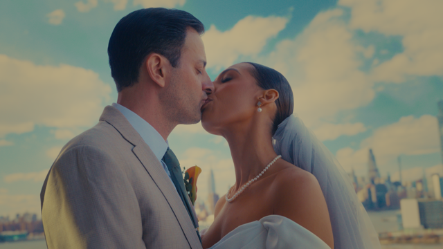 A couple kissing outdoors on their wedding day with a city skyline in the background.