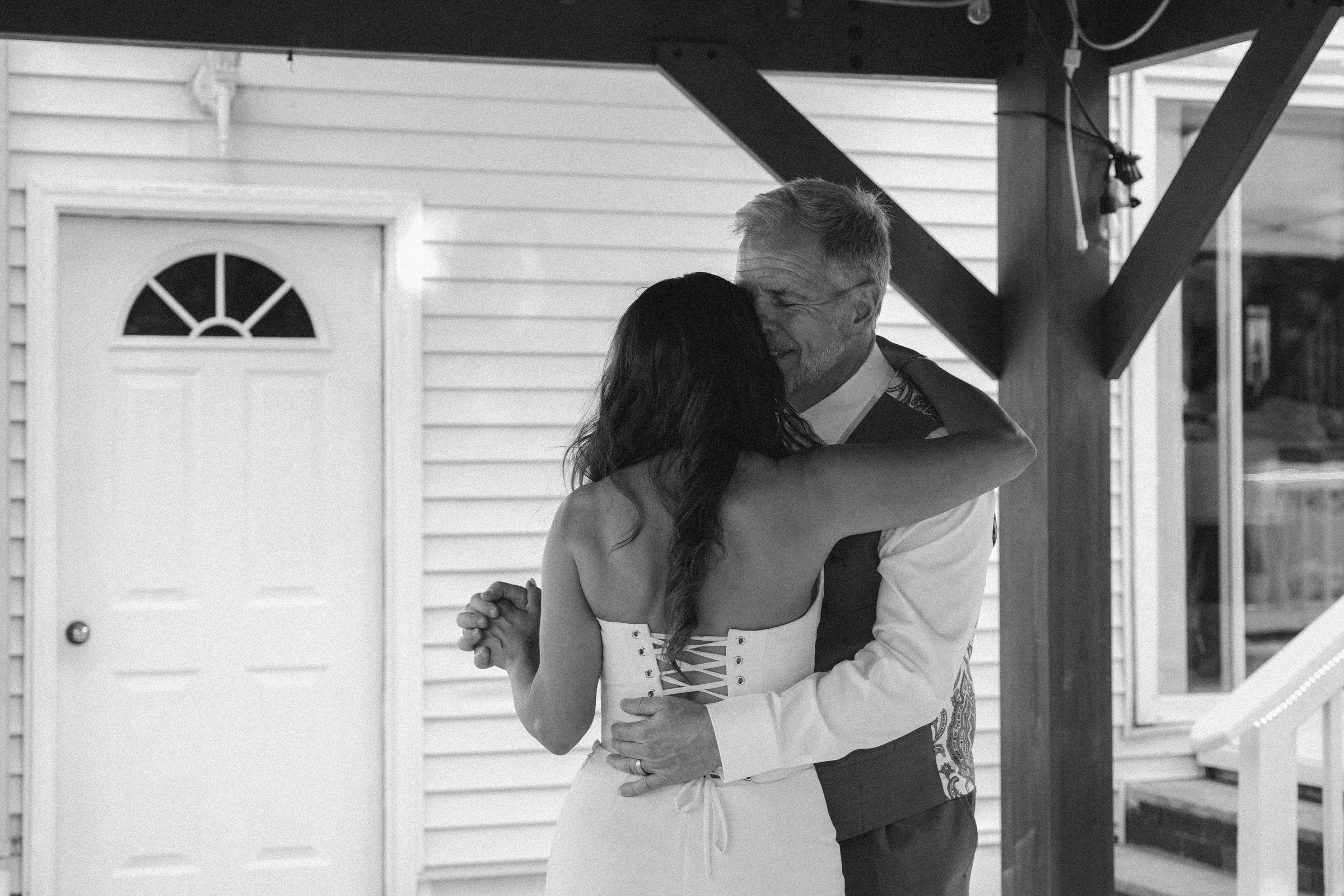 A couple dancing closely under a porch, smiling and embracing each other.