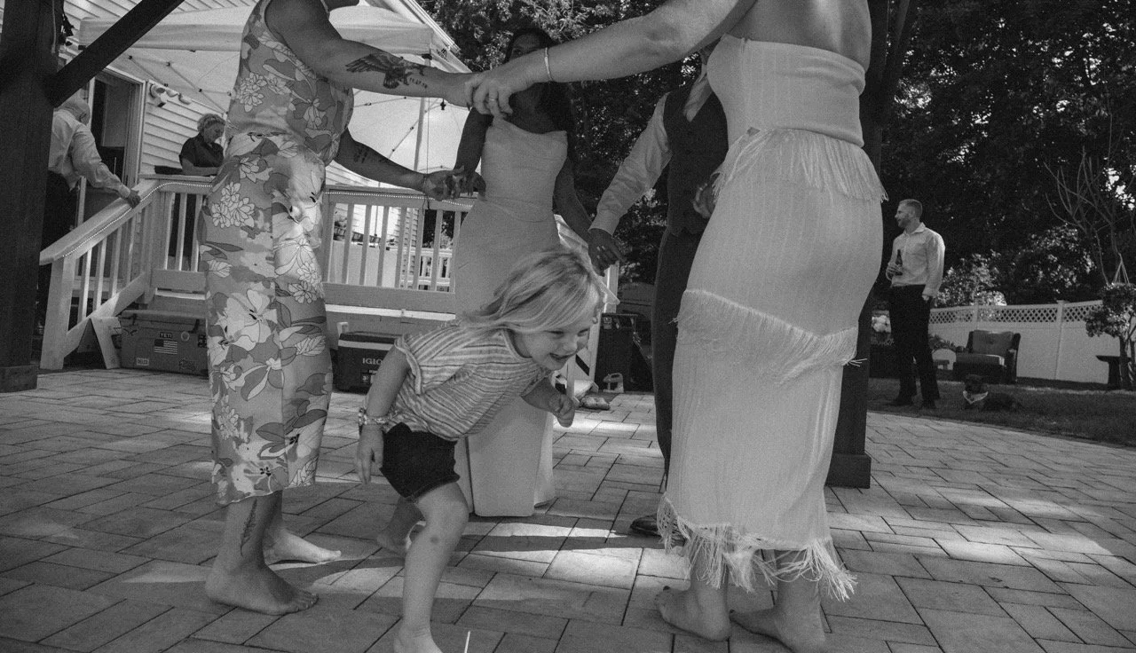 Children and adults dancing in a circle outdoors at a party.