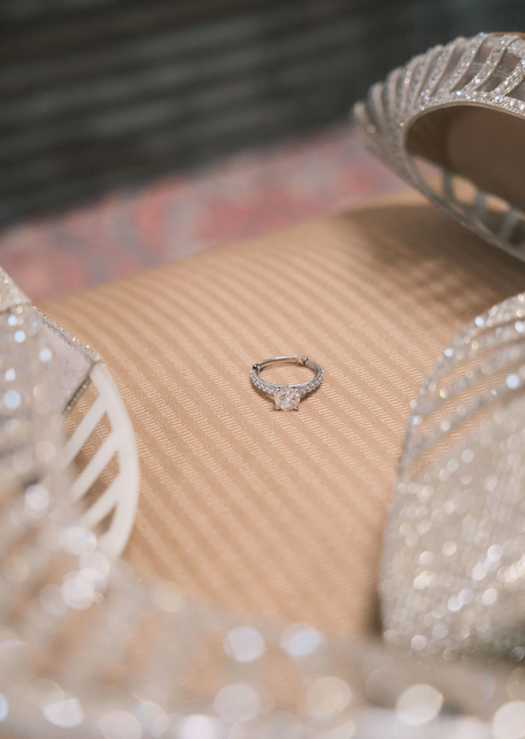 A diamond engagement ring inside a decorative jewelry box with a pink and beige lining, surrounded by a glittery, silver frame.