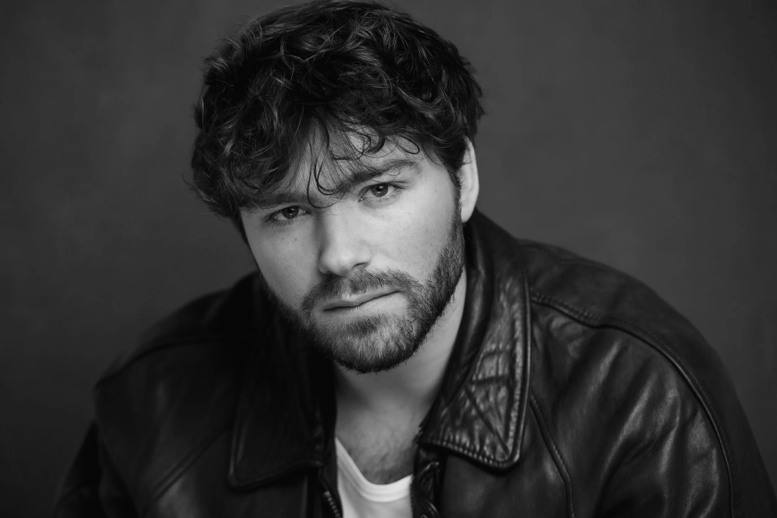 Portrait en noir et blanc de Raphaël Gareth avec une barbe et portant une veste en cuir, regardant vers l'objectif.