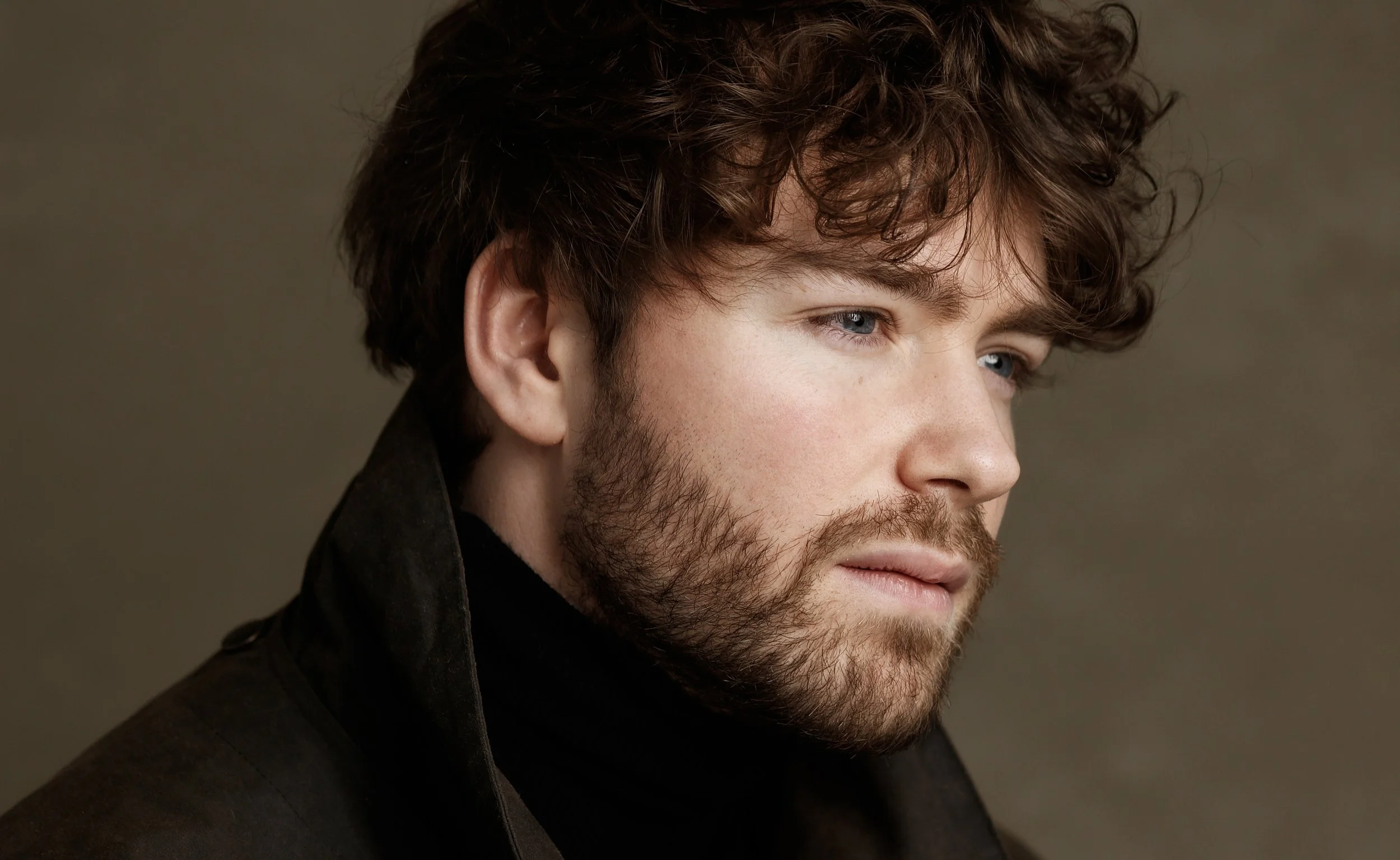 Portrait de Raphaël Gareth portant un manteau noir, regardant vers la droite, avec un fond neutre.