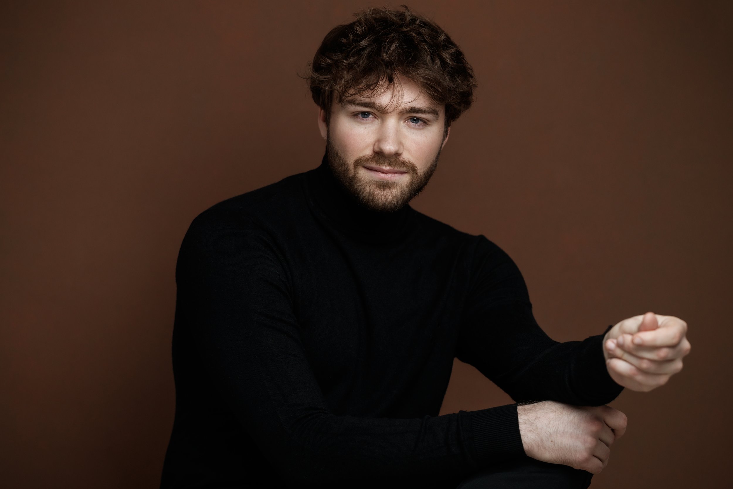 Raphaël Gareth portant un pull noir, posé contre un fond marron