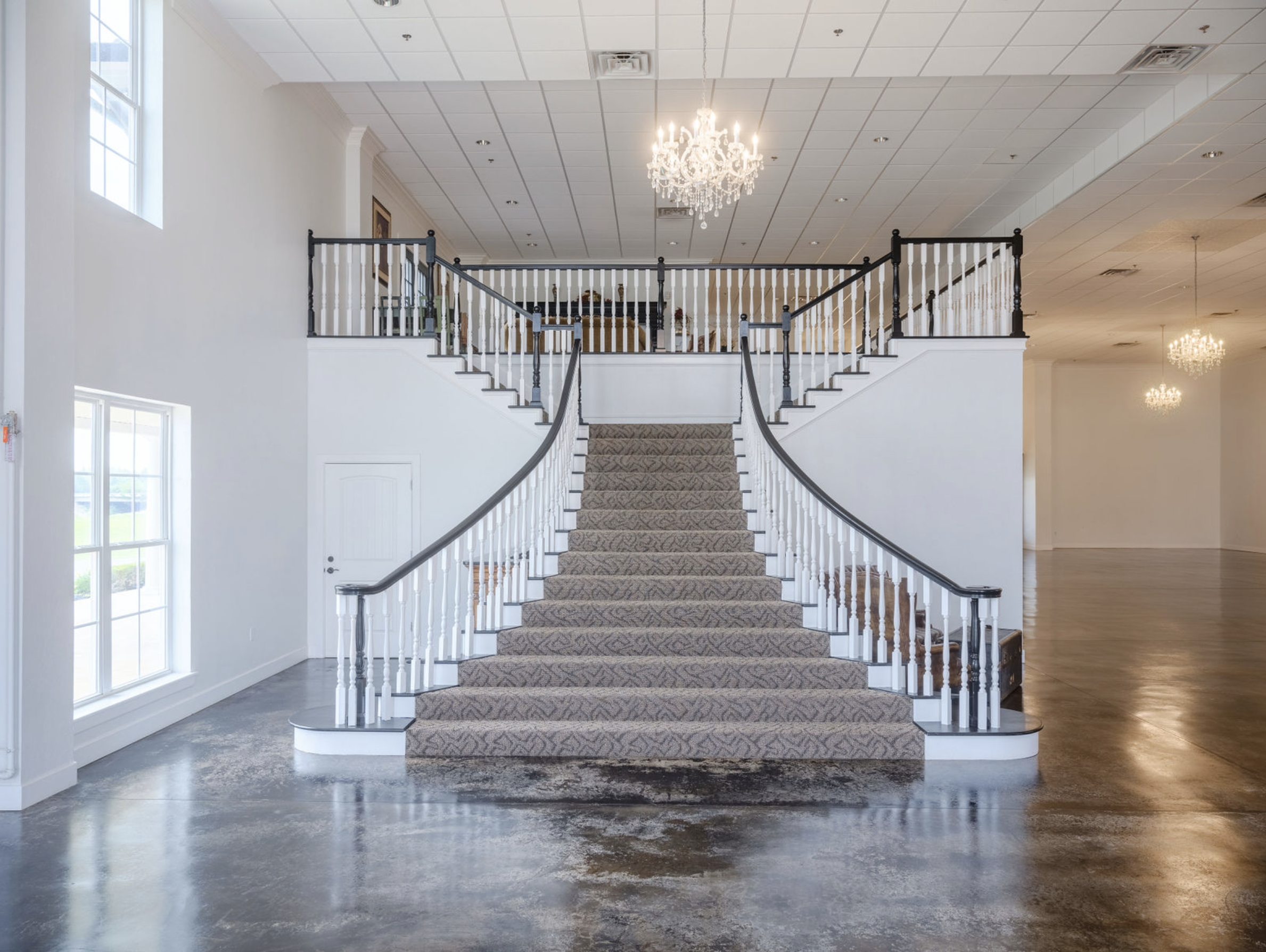 Elegant grand staircase inside Coal Creek Event Center featuring chandeliers, polished concrete floors, and spacious venue design perfect for weddings and special events.