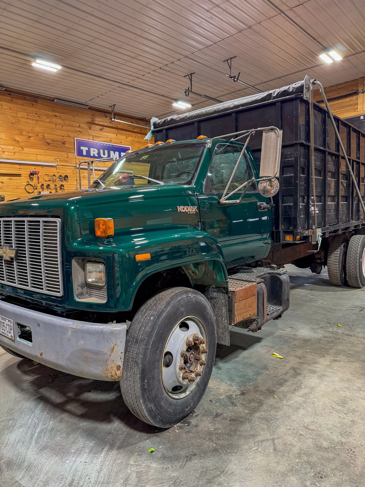 A green Chevrolet Kodiak truck parked inside a building with wooden walls and a Trump sign in the background. Tree Service Maine, Learned Tree Service 