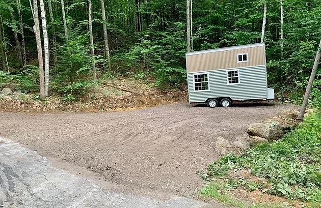 A small, two-story trailer parked on a cleared, dirt road in a forested area, with trees and green foliage in the background. Tree Service Maine, Learned Tree Service 