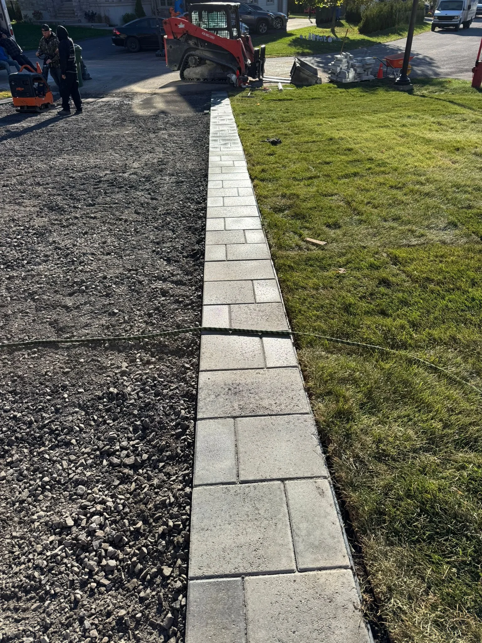 Travaux de pose de pavés le long de un trottoir avec des ouvriers et des machines de construction sur un chantier urbain.