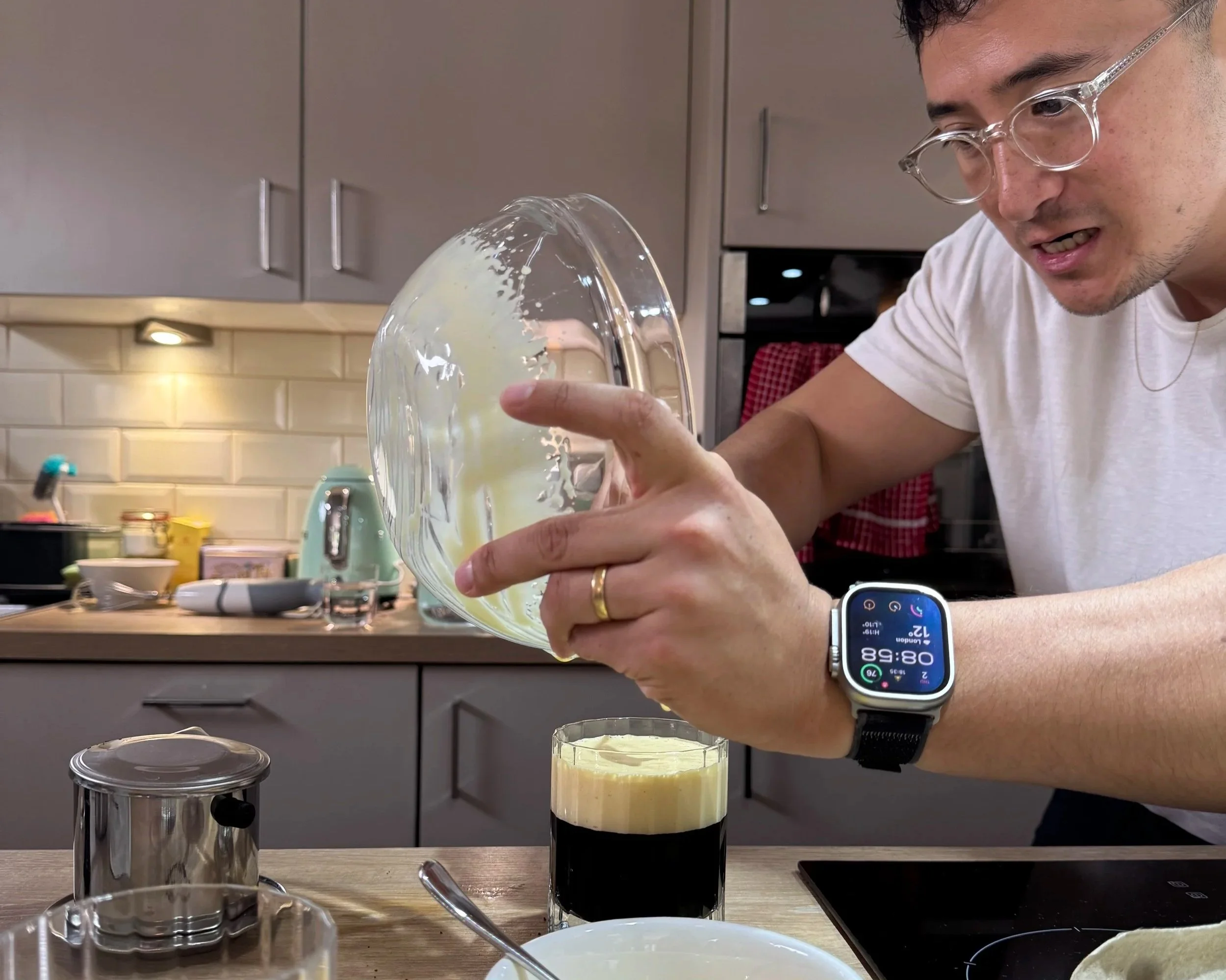 A man pouring a yellow liquid into a glass of dark beer in a kitchen.
