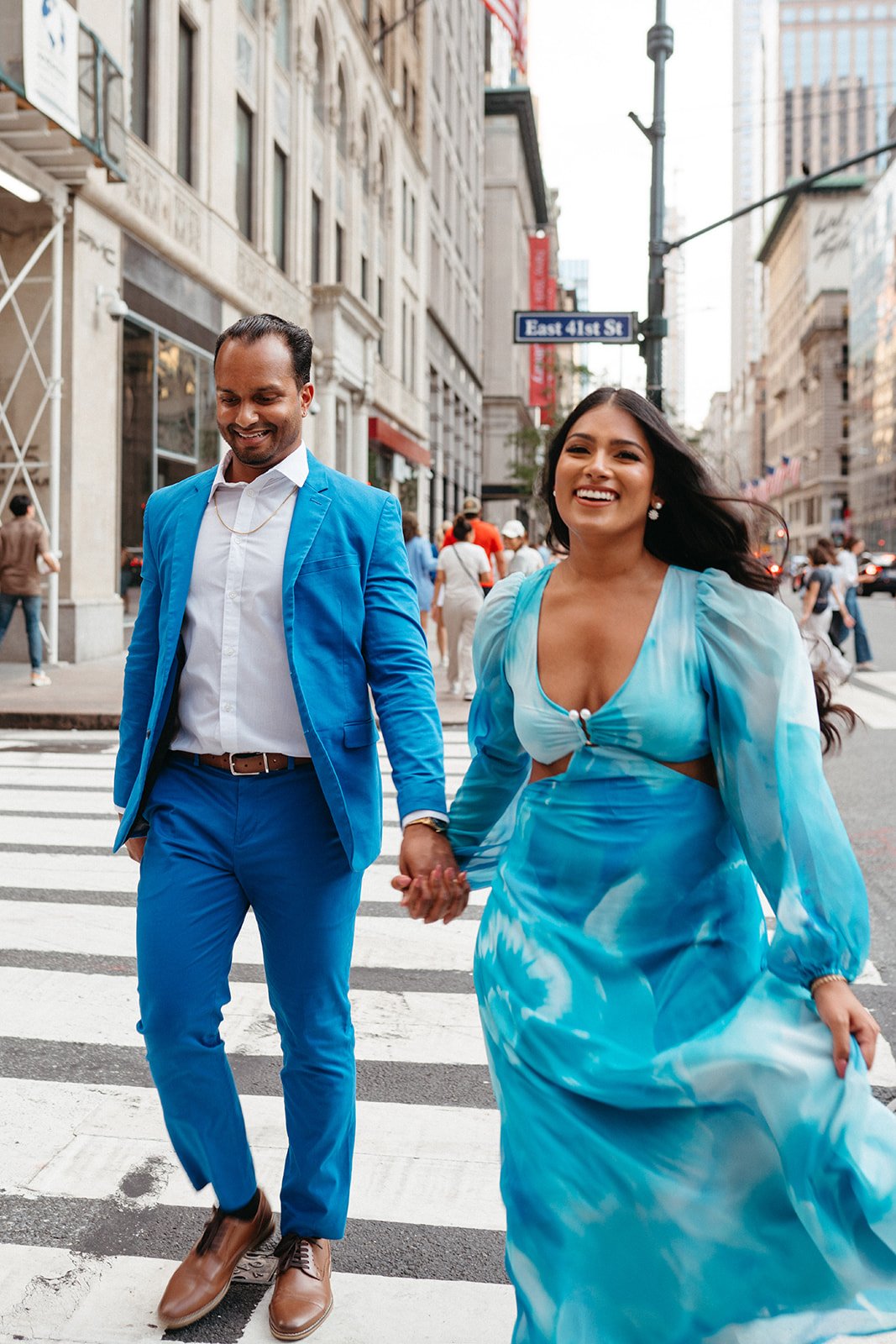 Outdoor nighttime dining setup with a long table covered in a white tablecloth, decorated with flowers, glassware, and bottles, surrounded by white chairs, with trees and bushes illuminated in the background.