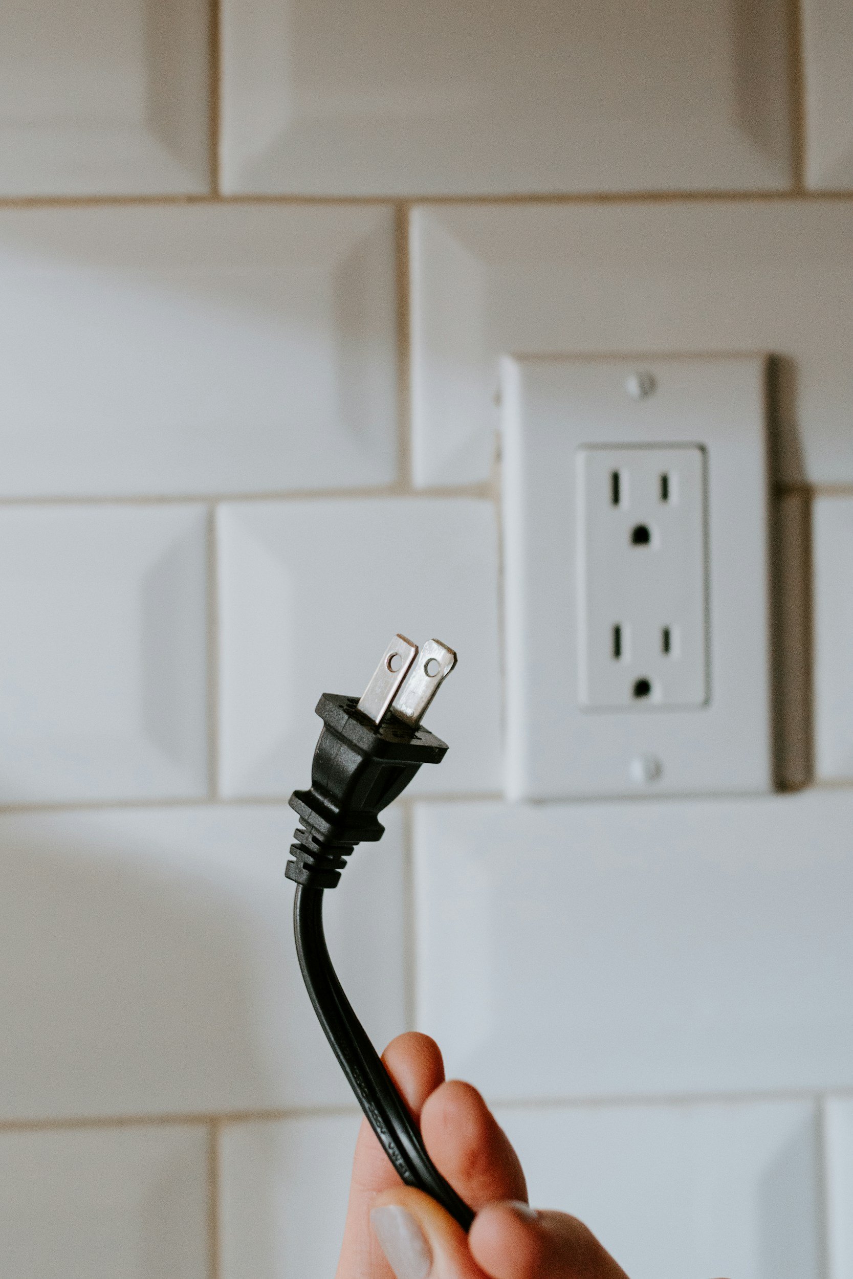 hand holding a male plug-in in front of a kitchen outlet