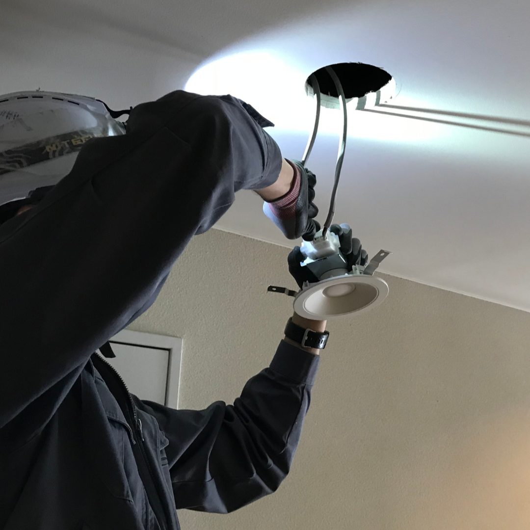 A person installing a ceiling light fixture, holding the fixture's base and wiring it into the ceiling.