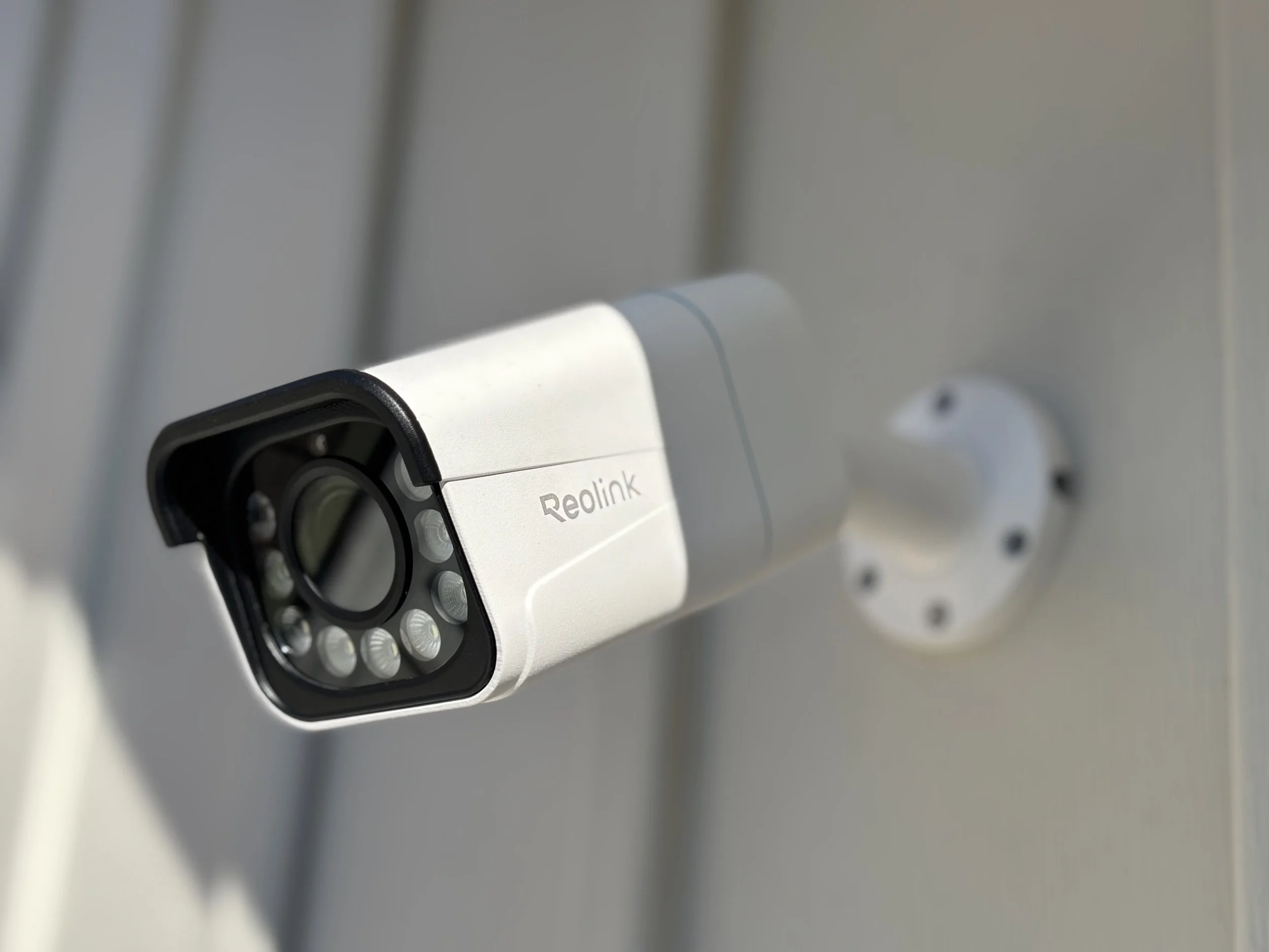 Security camera mounted on a wall with a white and gray casing. Demonstrating security system installation including camera and motion lighting.