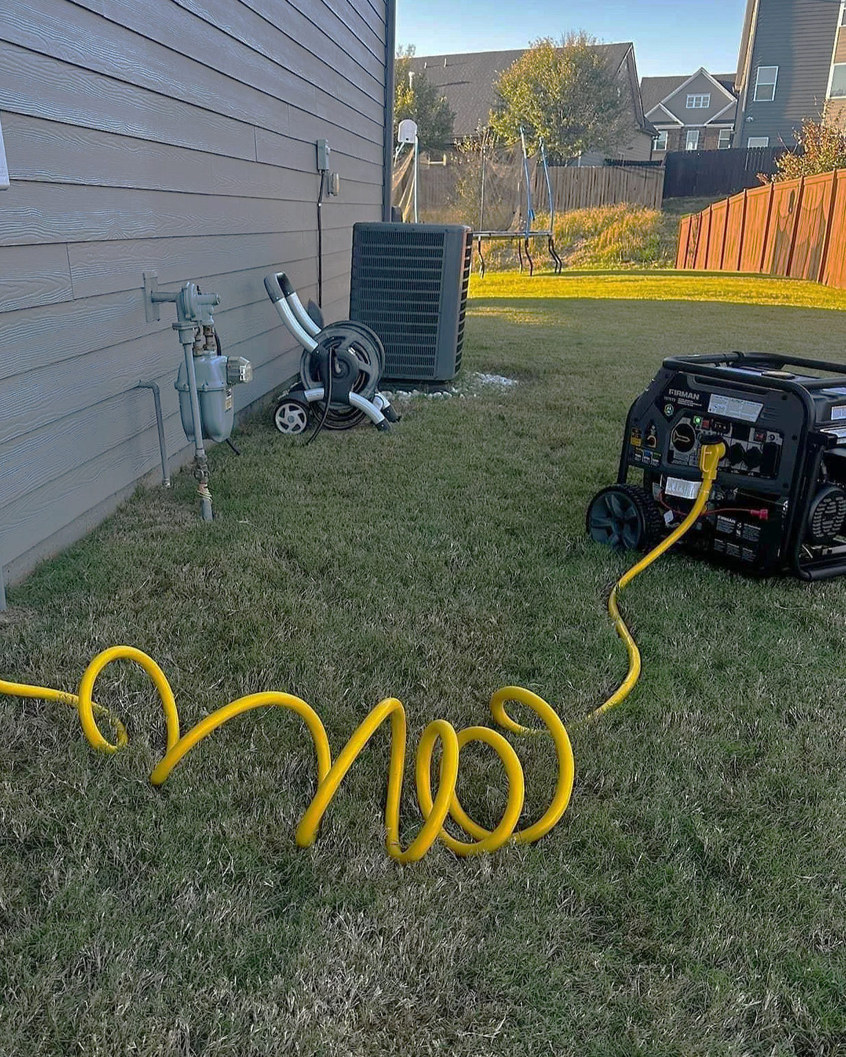 Backyard with a generator, air conditioning unit, garden hose, and an inflatable trampoline in the background.