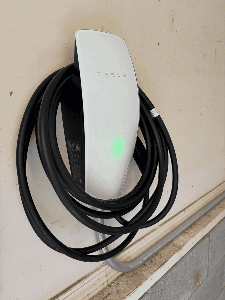 Tesla electric vehicle charging station mounted on a wall with a charging cable coiled around it. Demonstrating Tesla charger installation services.