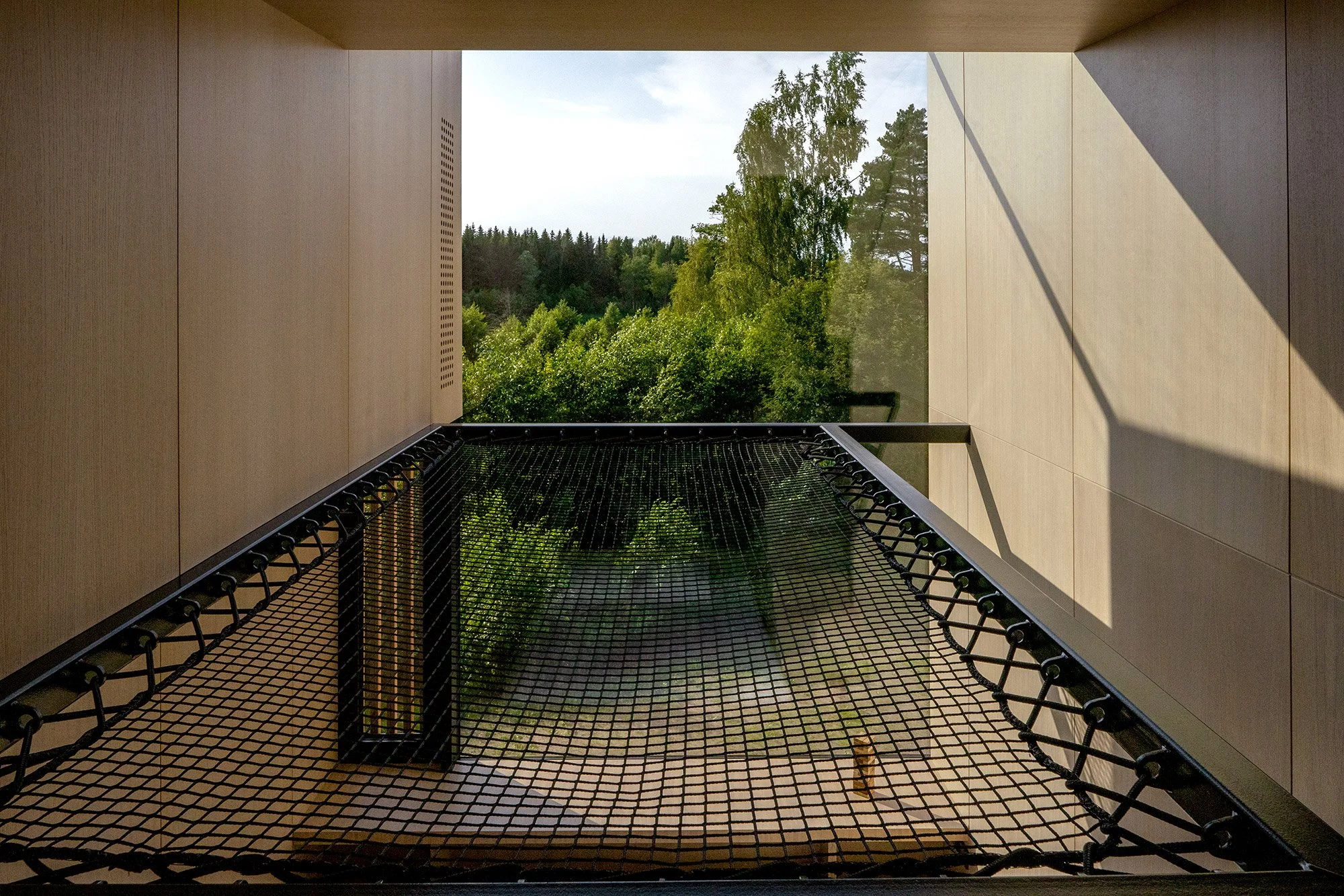 View of a natural green landscape from a suspended hammock mezzanine net, set within a timber-lined warm and welcoming treehouse-inspired interior