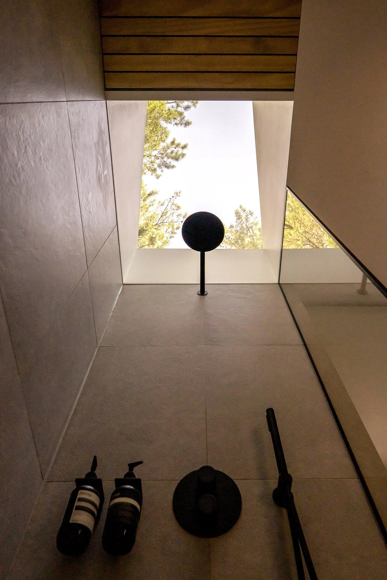 Looking up the skylight of a contemporary shower room, with dappled natural light filtered by trees elevating the daily morning rituals in a pre-fabricated modular contemporary retreat within nature