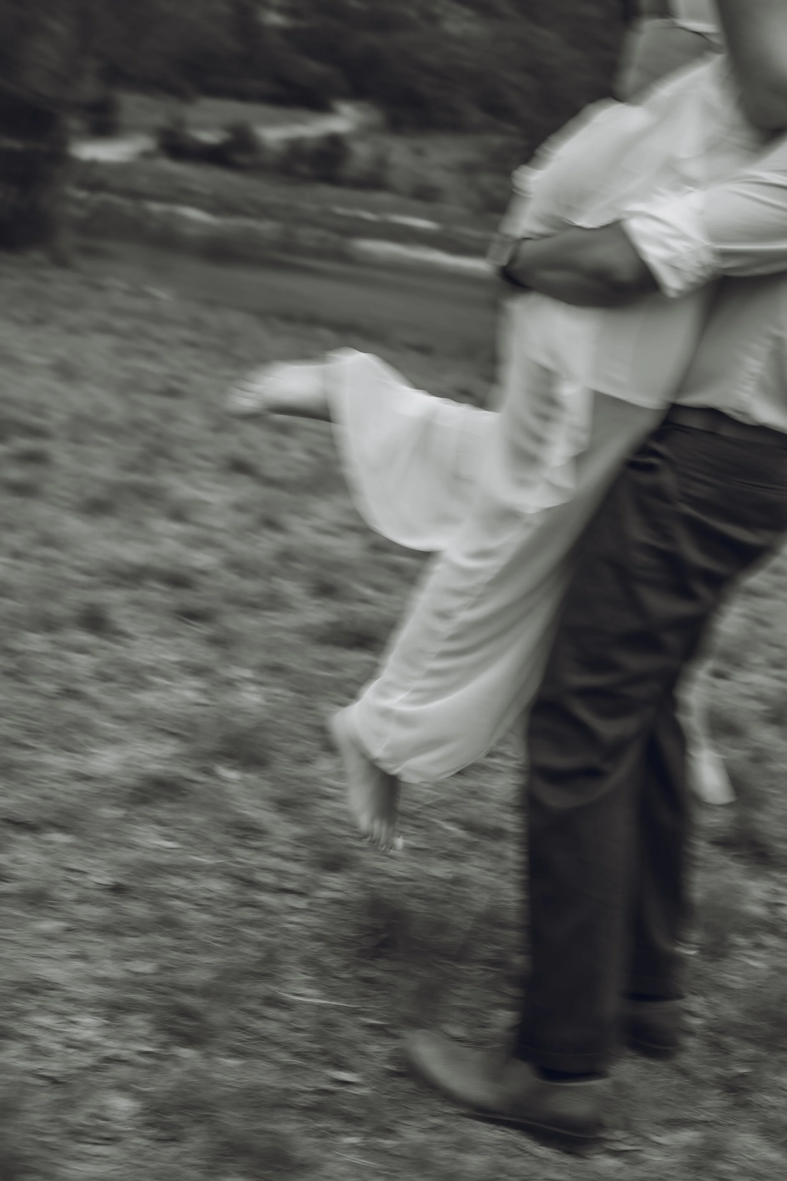 A person wearing dark pants and shoes carrying another person in a white outfit through a grassy area.