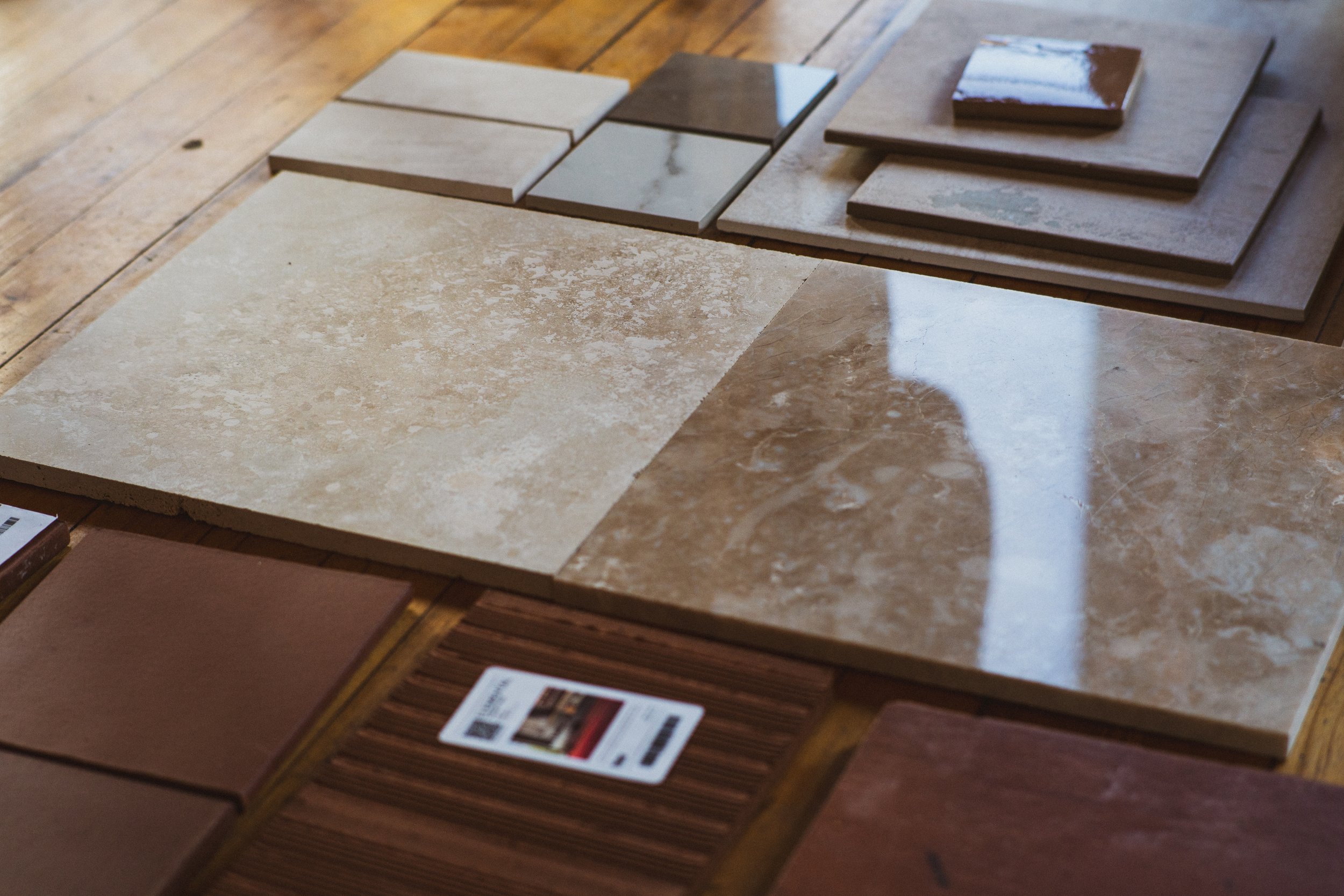 Display of various ceramic and marble tile samples on a wooden surface.
