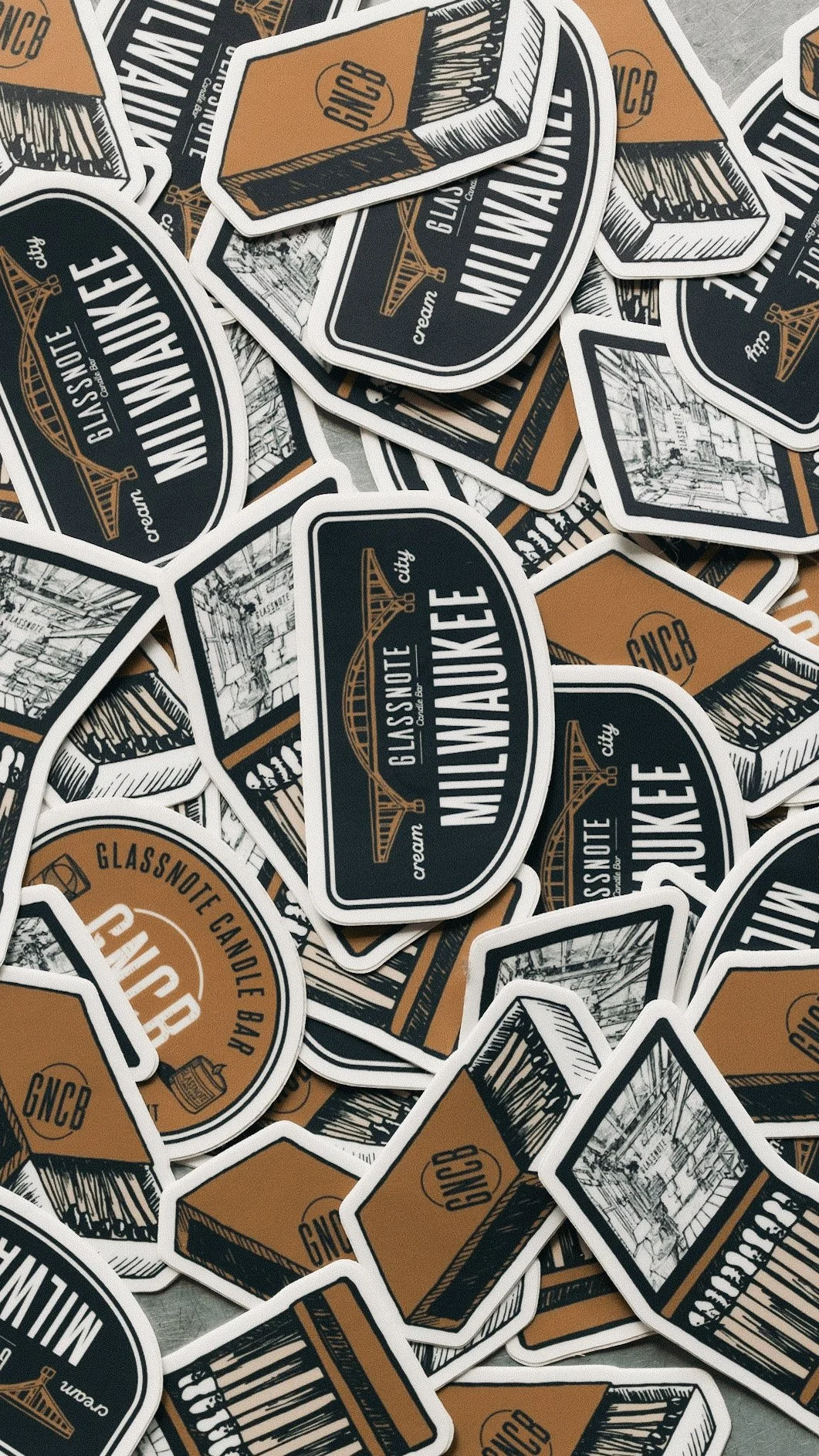 A pile of glassnote candle bar merch stickers featuring the text 'Milwaukee City' and illustrations of bridges and cityscape in orange, black, and white colors.