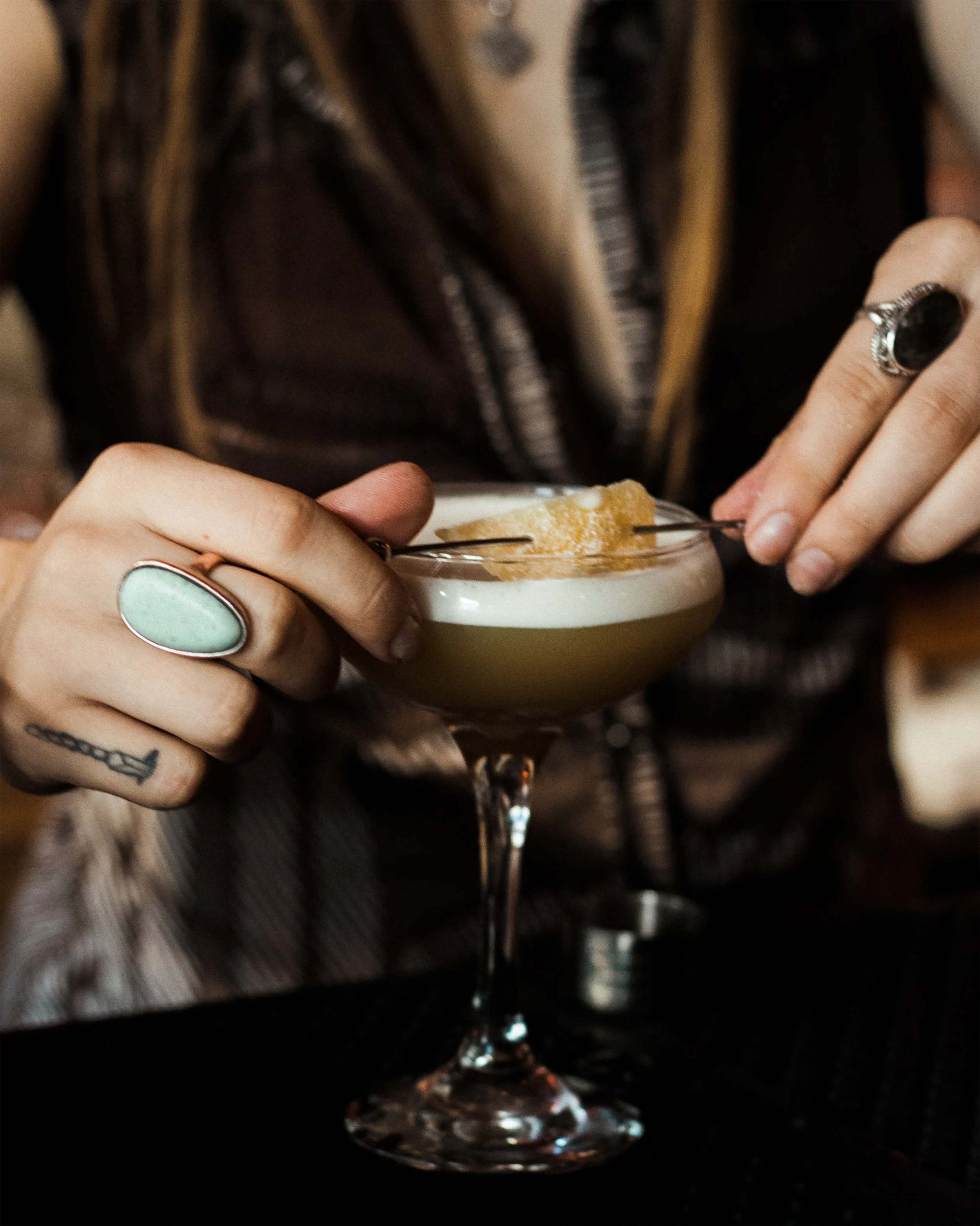Person garnishing a craft cocktail with a lemon slice at the zinc bar.