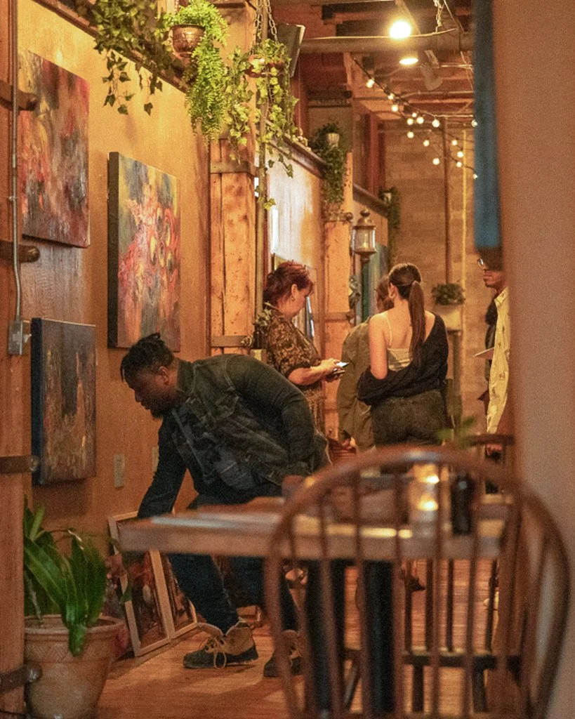 People sitting in the cozy hallway with warm lighting and local art featured on the wall of the candle bar. 
