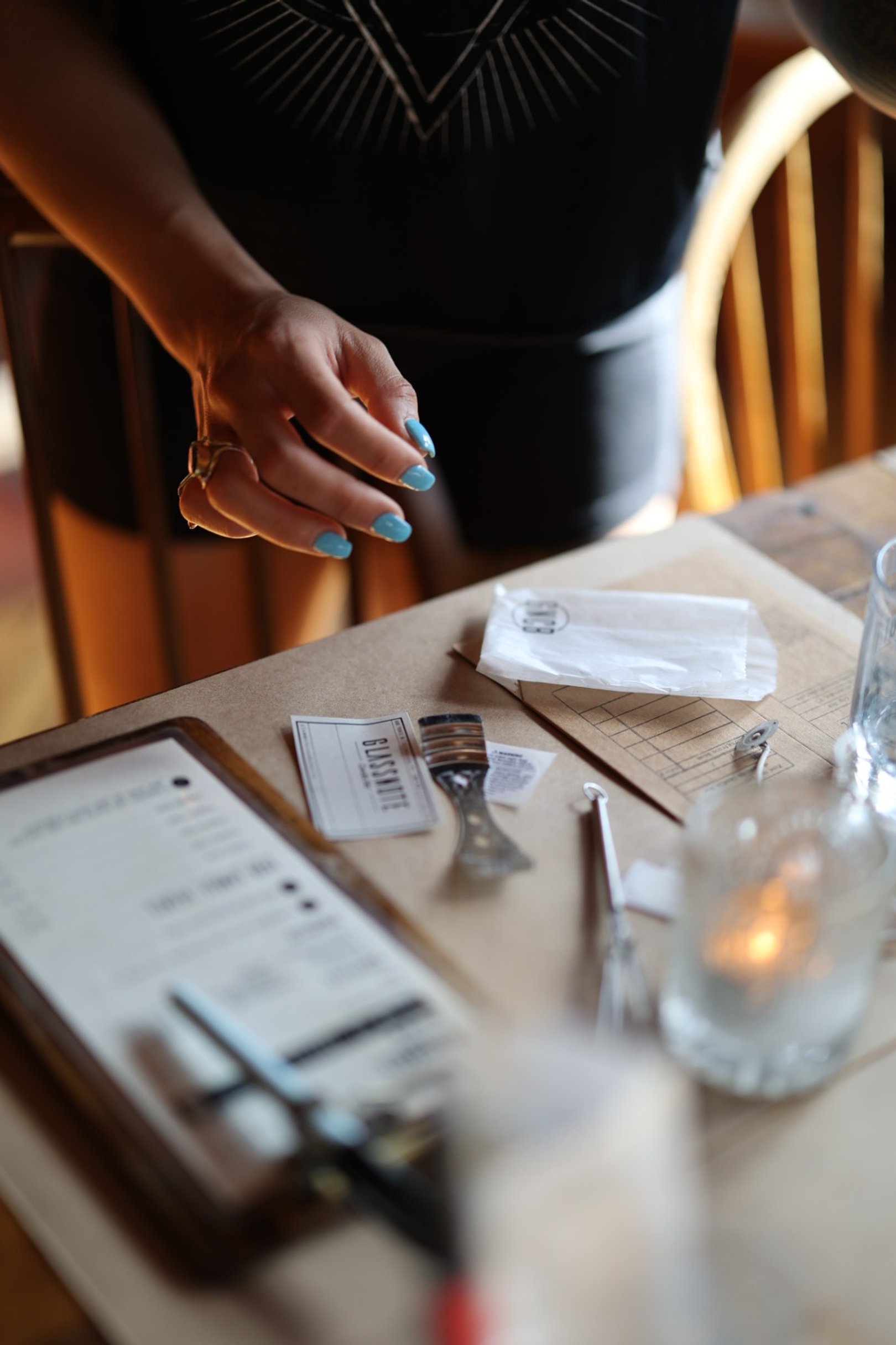 A person with blue painted nails and gold rings sets the table for the candle making experience at glassnote candle bar. 